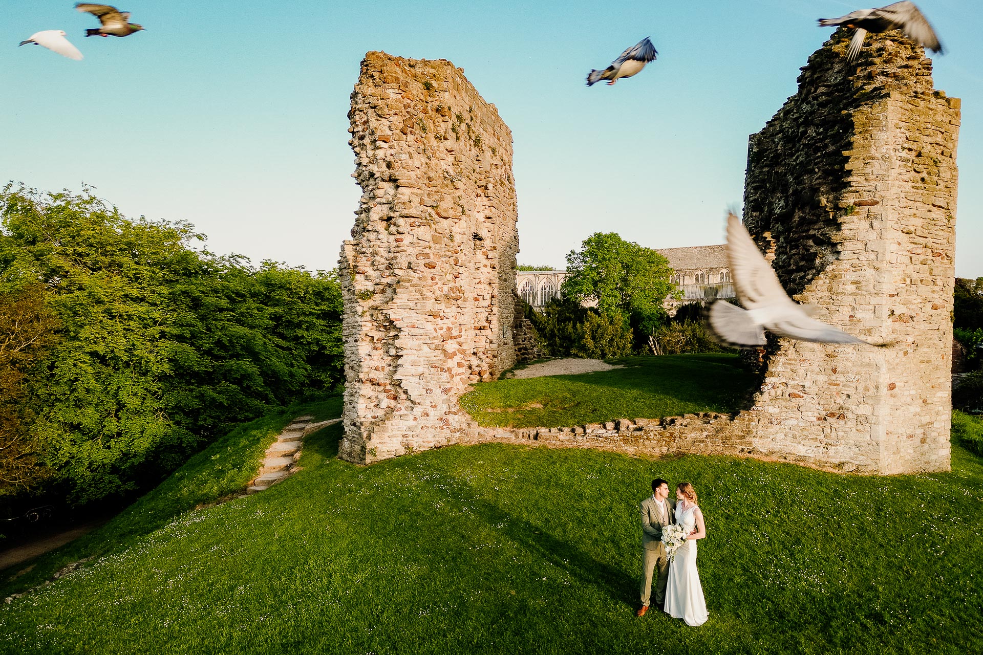 Drone wedding photography captures pigeons in flight above a couple at a ruined castle. By Dorset wedding photographer Nathan Eames