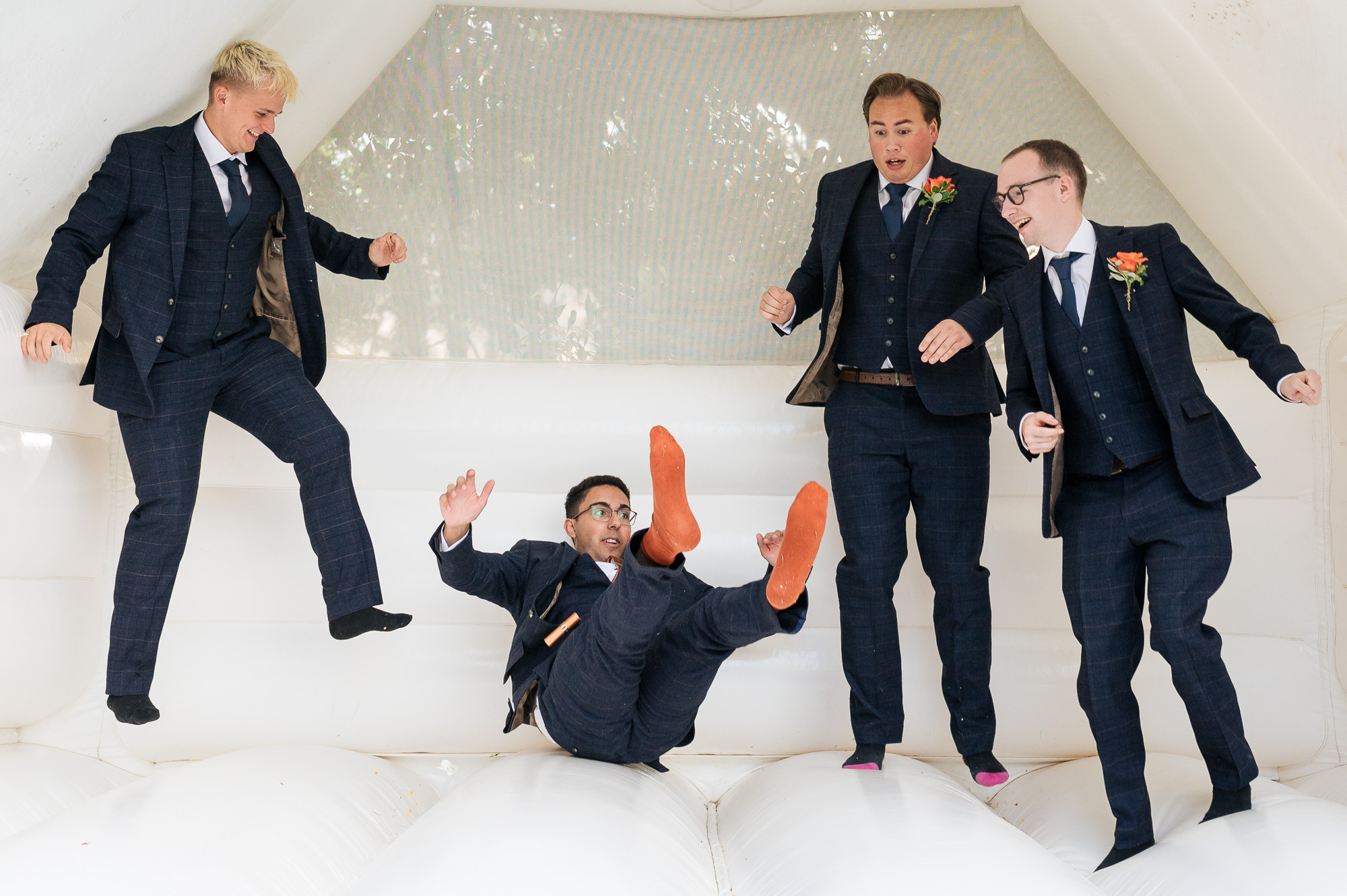 Bouncy castle moment as one groomsman lands on his bum, orange socks in the air. 3 others are mid-jump. By Libra Photographic in Dorset