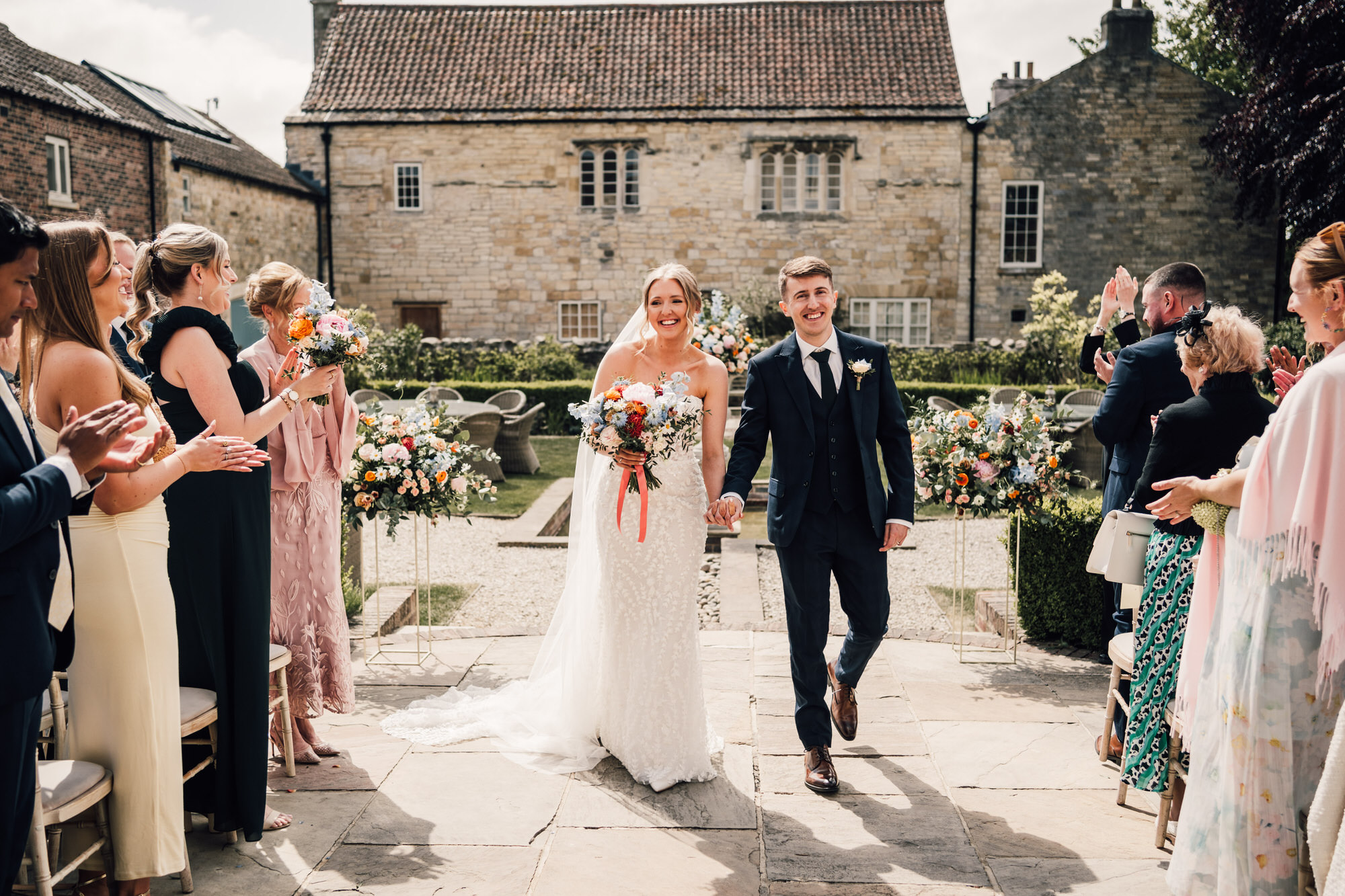 Newlyweds turn and walk between their guests to a standing ovation at Priory Cottages wedding venue - relaxed wedding photography moment captured in Yorkshire by David Lindsley Photography