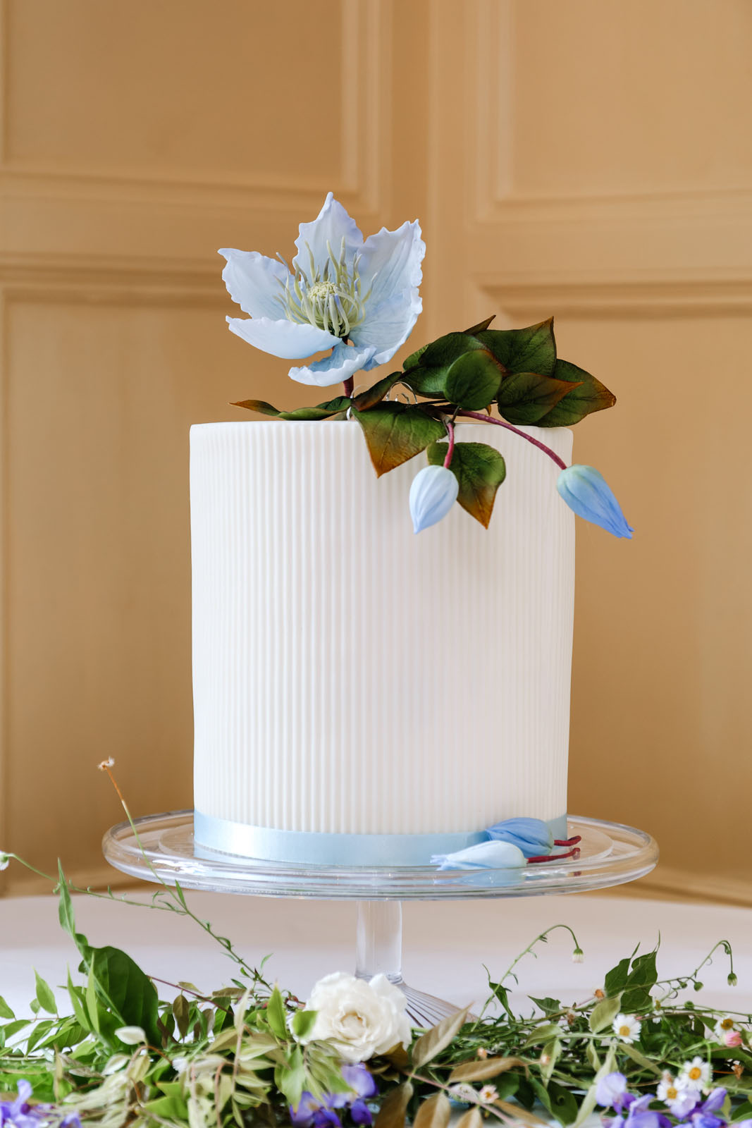 Simple single tier wedding cake with pristine white icing and blue sugar paste clematis