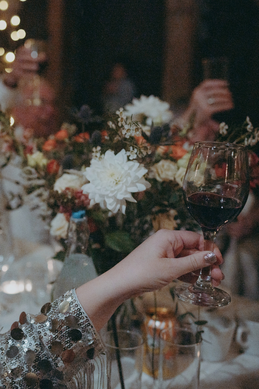 A woman's hand raising a wine glass across wedding tables with dahlia centrepieces - by Damien Vickers Photography