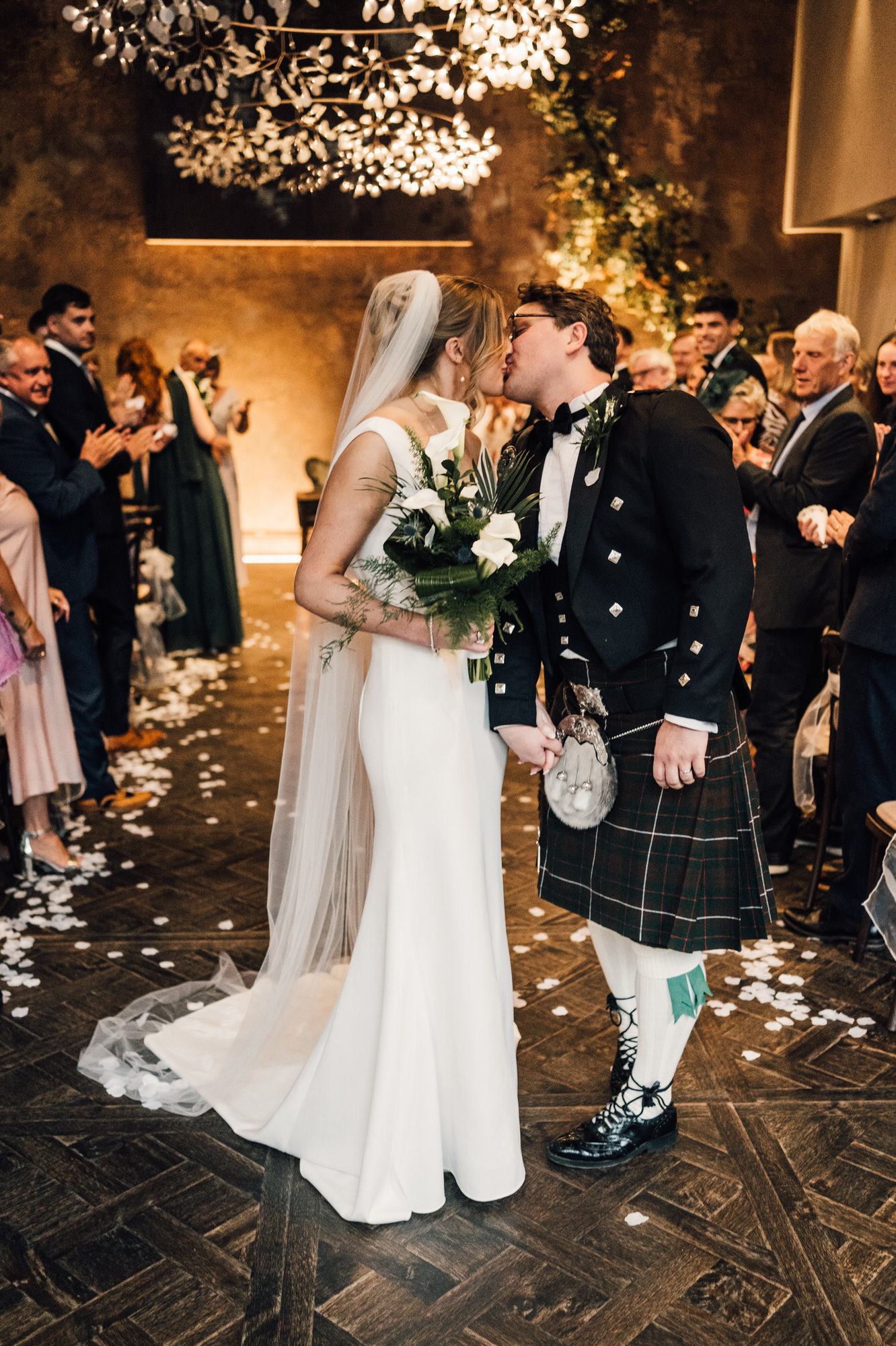 Newlyweds kiss under contemporary chandeliers at Manor House Lindley Hotel. By Yorkshire wedding photographer David Lindsley