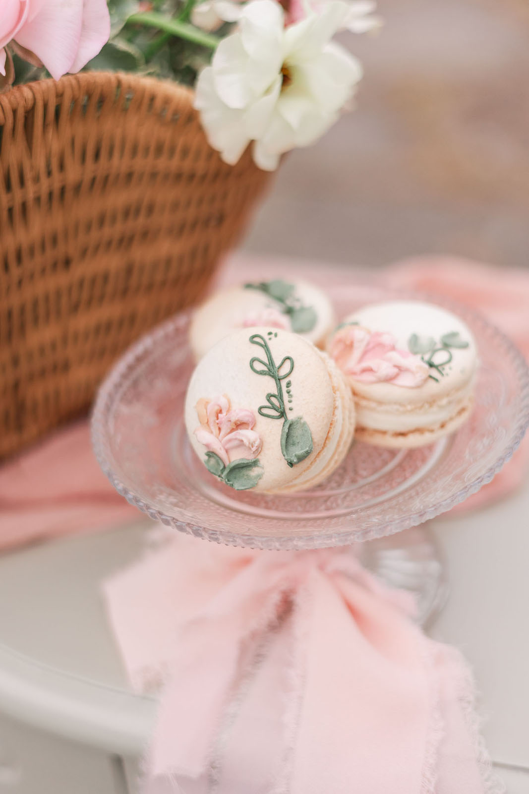 three flower decorated delicate pink macarons on a glass serving plate, tied with silk ribbon.