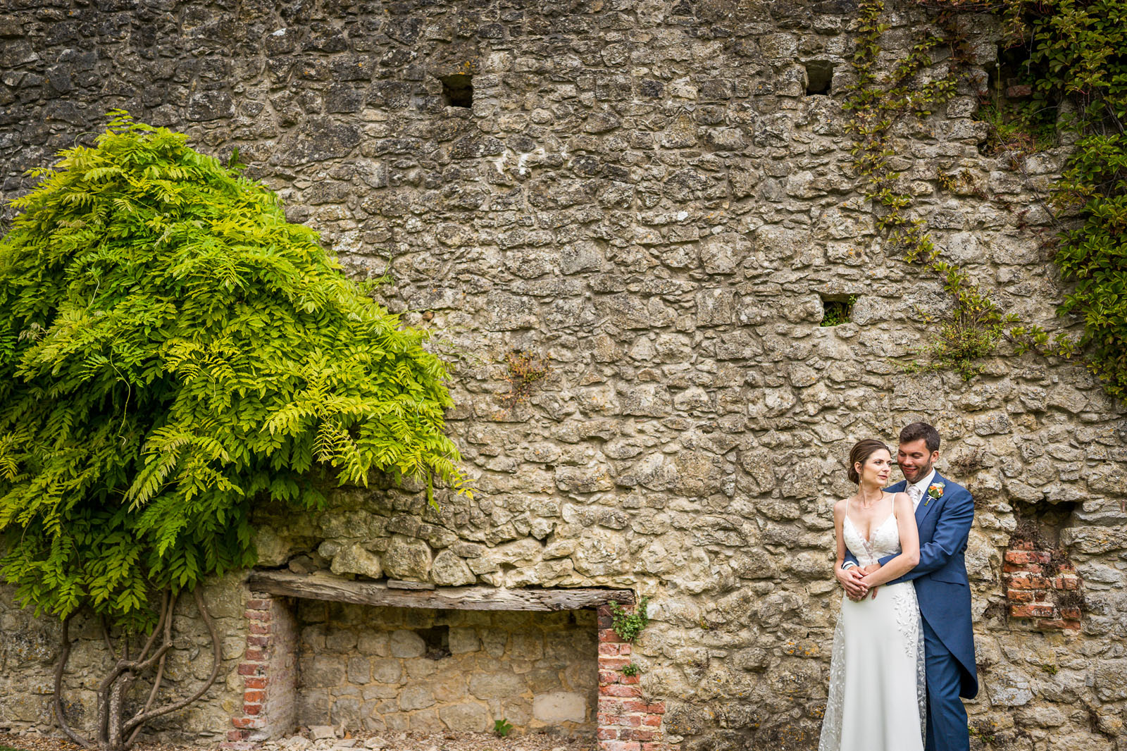 Ancient stone walls at Westenhanger Castle as a bride and groom pose for a portrait - Benjamin Toms Photography | Kent