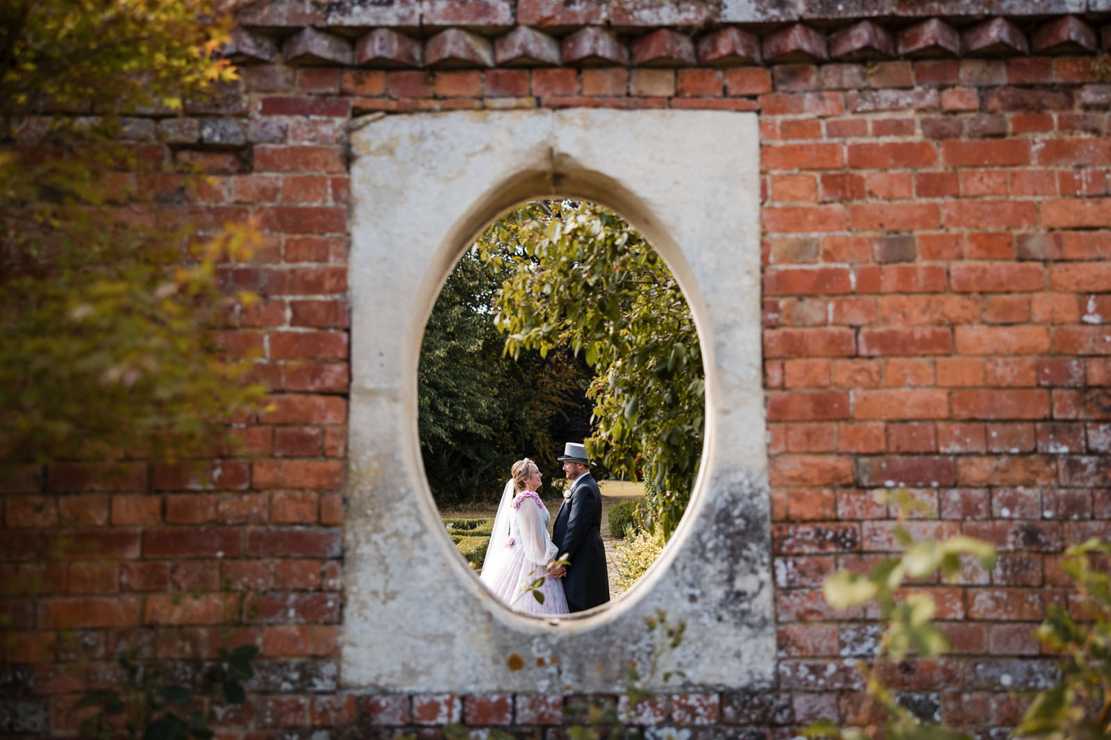 Artistic wedding photography using a feature brick wall with oval cutout to frame a bride and groom having a private moment to themselves on their wedding day - by Greg Shingler Photography
