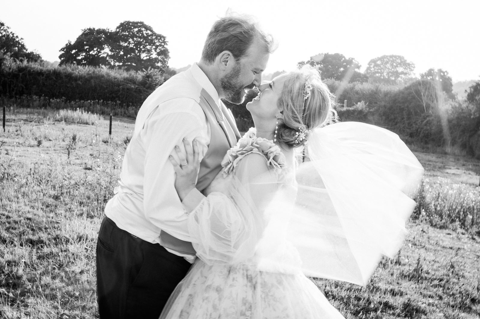 groom and bride about to kiss - he's wearing a shirt and waistcoat, and she's in a floral dress with a veil. Beautiful black and white image by Greg Shingler Photography