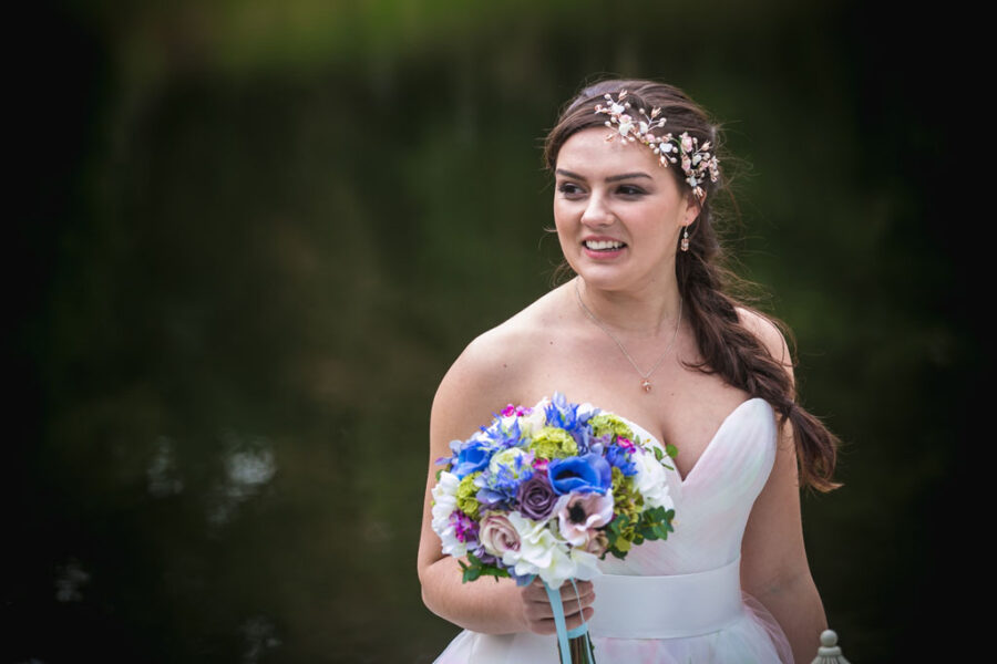 Bride carrying a compact bouquet of spring flowers with anemones in blues and pinks, wearing a strapless white dress and delicate floral hair accessory by Emma Rose Treasures