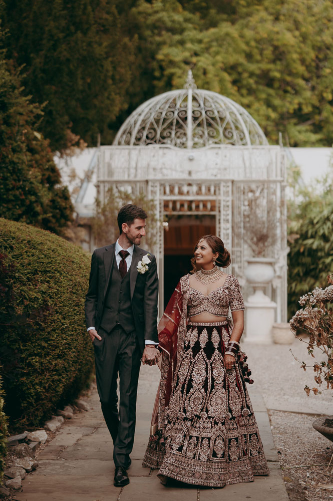 Groom and bride at Coombe Abbey. He's wearing a suit and tie and she's in burgundy and gold Indian dress | luxury editorial wedding photography by Damien Vickers Cambridge
