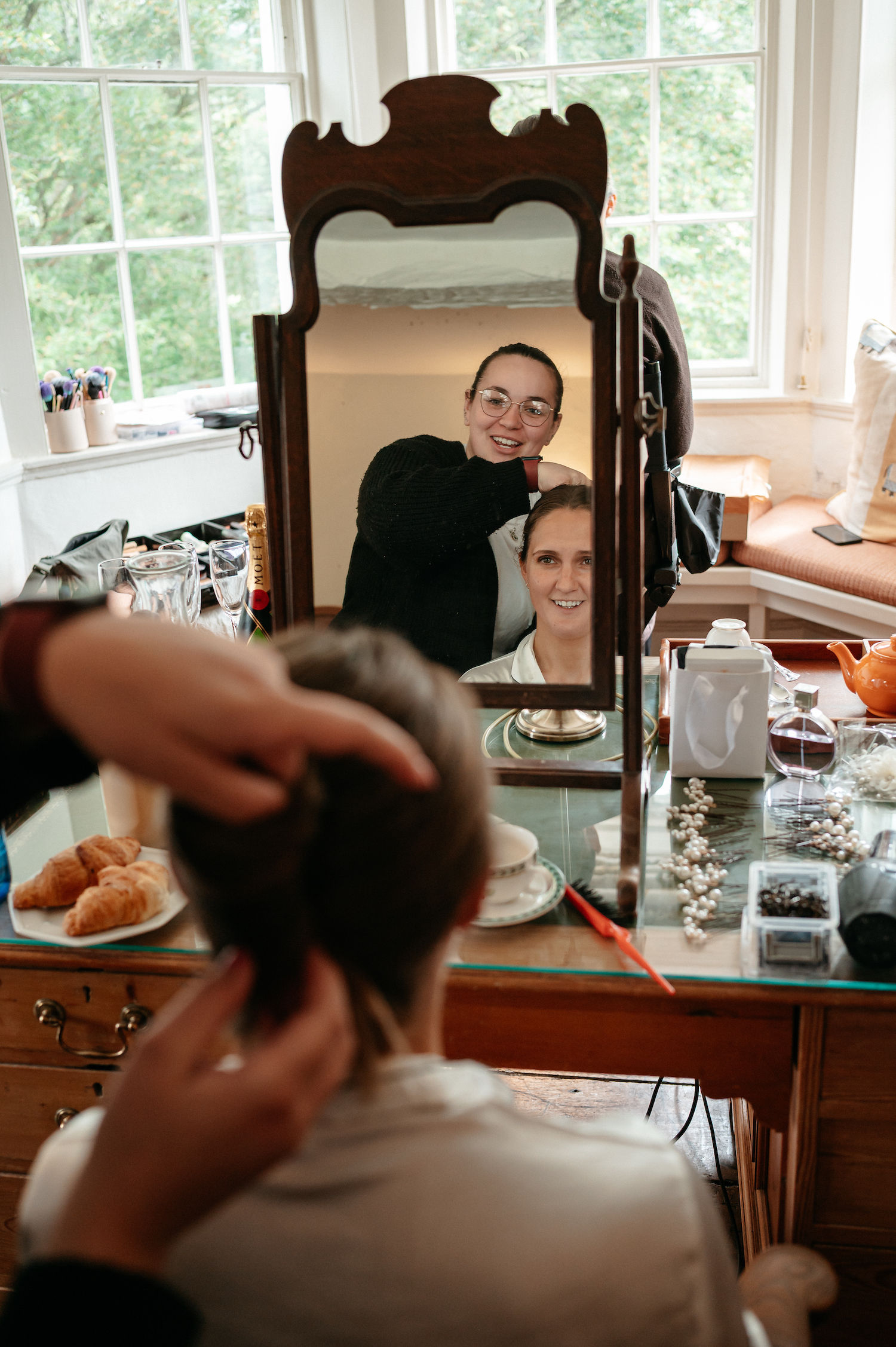 Wedding hair and make up artist at work reflected in the mirror over her bride's shoulder