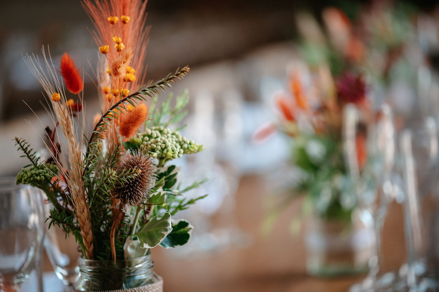 Autumnal coloured wedding flowers, grasses and seedbeds in jam jars