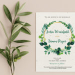 Example of a wedding invitation by Little Green Wedding, placed alongside a sprig of eucalytpus. The invitation has green floral wreath with the couples names in the centre and text above and below