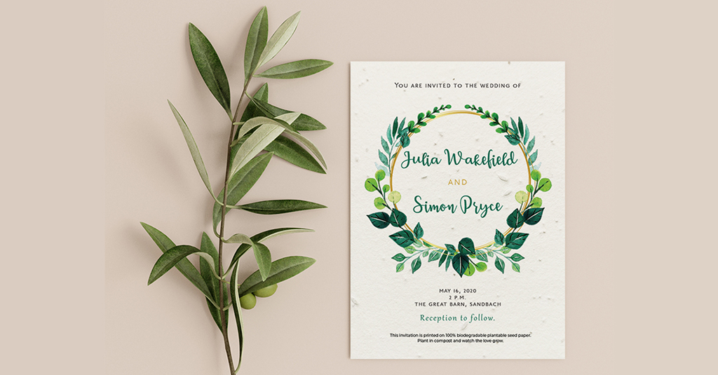 Example of a wedding invitation by Little Green Wedding, placed alongside a sprig of eucalytpus. The invitation has green floral wreath with the couples names in the centre and text above and below