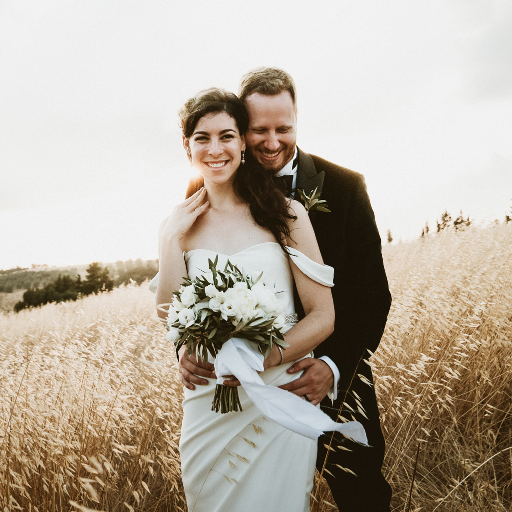 Boho bride and groom in a field of grass, by Benni Carol Photography