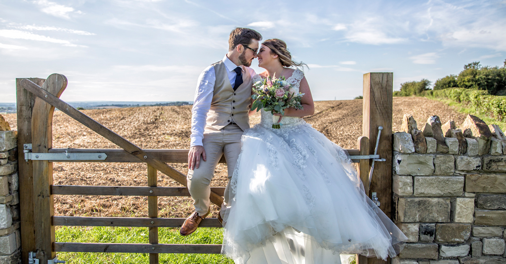 A bride and groom sit on a gate in the Yorkshire countryside - image by Daze Photography