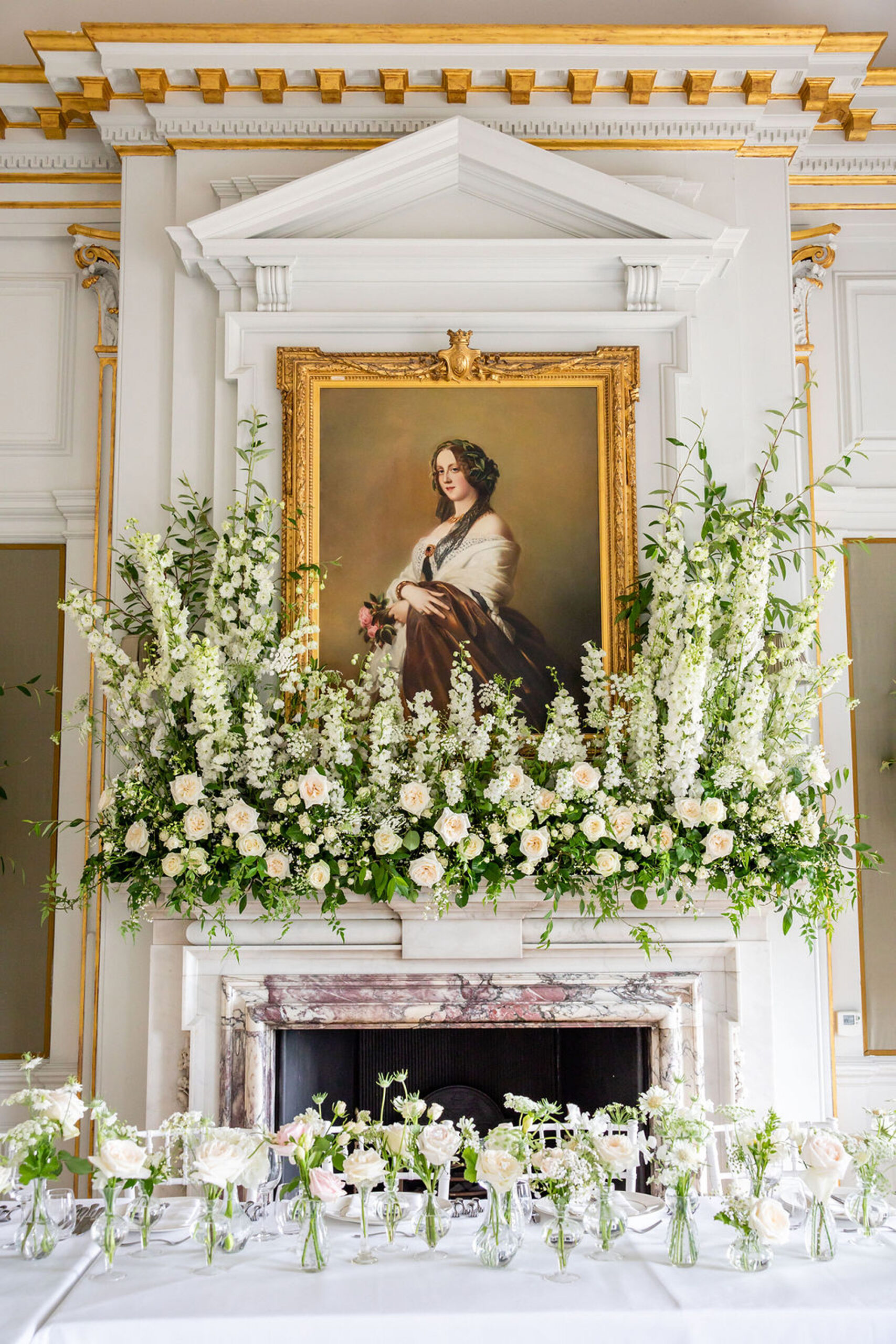 Elegant green and white floral display by Niemierko on a marble fireplace with a regal looking portrait in a gilt frame on the wall behind