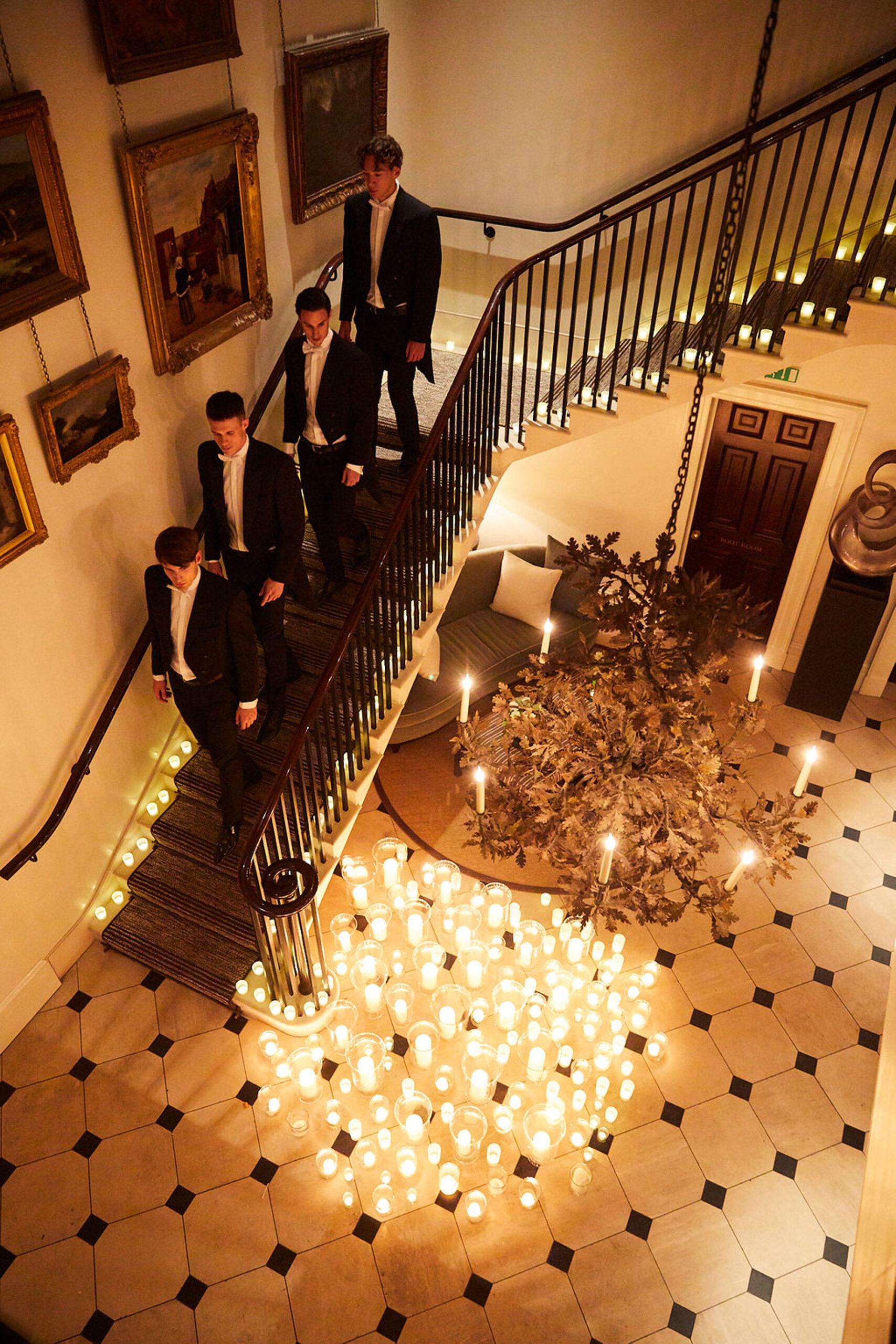 Looking down onto a grand staircase in a luxury venue, with Niemierko hosts walking down the stairs in suits, and hundreds of candles on the floor below making a beautiful display