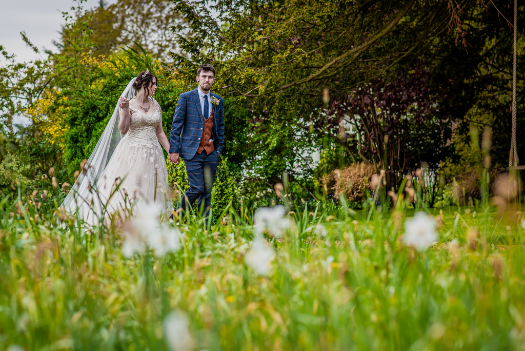 Photo of Lorna and Keanu's wedding at Stradsett Hall. The venue is quirky with lots of foliage and greenery. There are 30 guests and the couple are in a blush wedding dress and blue check suit. Photography by Damien Vickers.