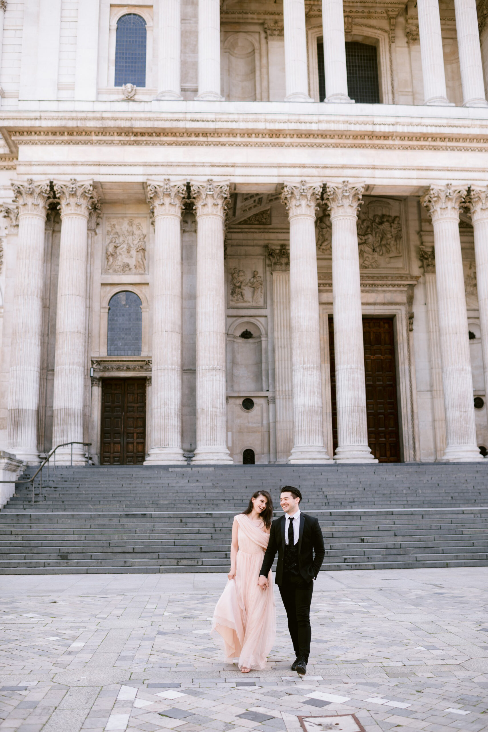Katia and John photographed by St Paul's Cathedral in London. She wears a pale coral longline off the shoulder dress. He's in black tie and suit. Captured by Eva Tarnok Photography