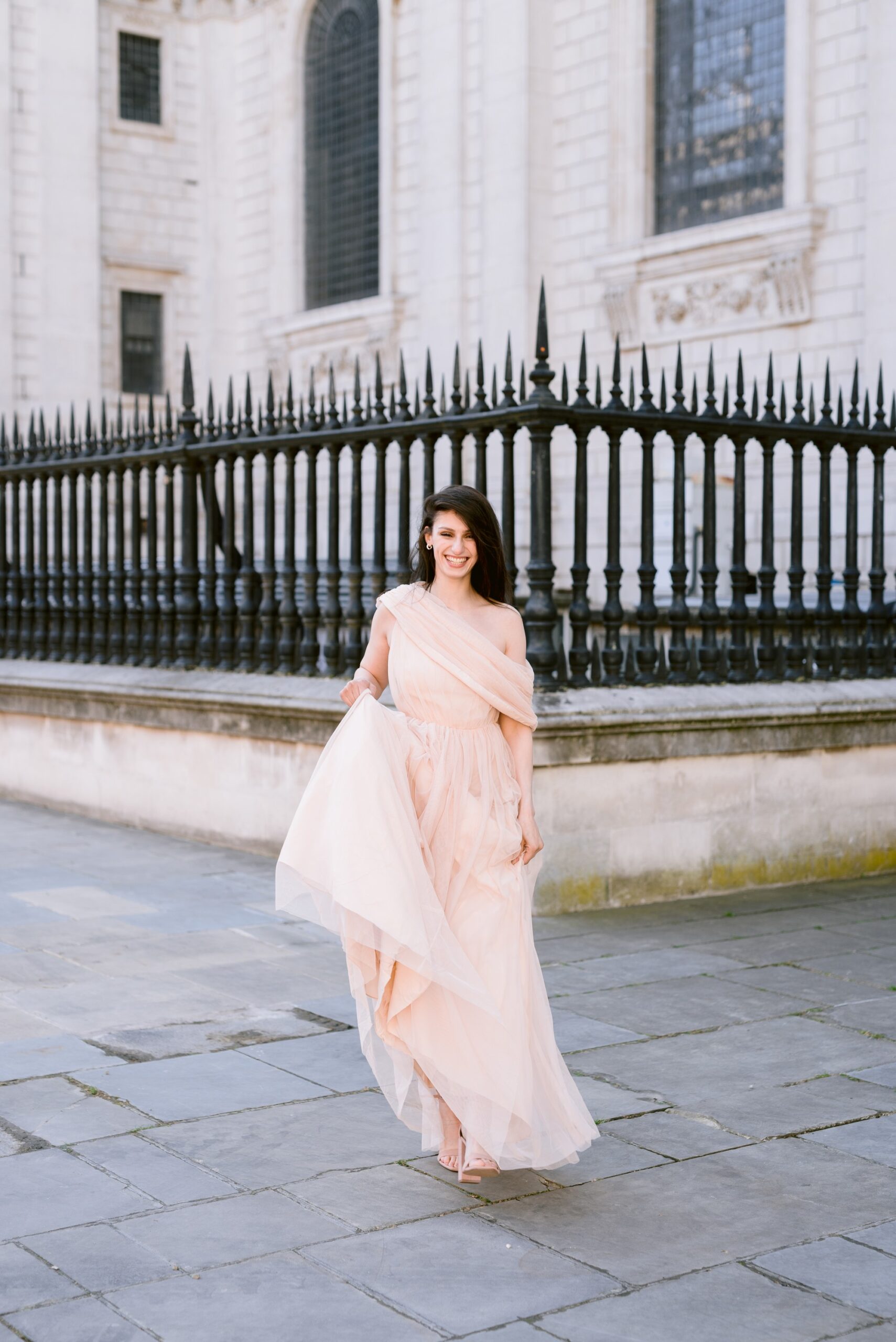 Katia and John photographed by St Paul's Cathedral in London. She wears a pale coral longline off the shoulder dress. He's in black tie and suit. Captured by Eva Tarnok Photography