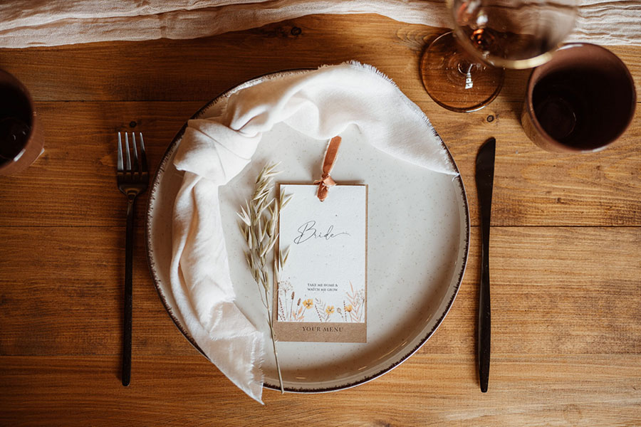 A ceramic plate on a wooden table. There's a knotted napkin and a pretty place name with a velvet ribbon. Photographer credit Sarah Hoyle, styling by Amethyst Weddings