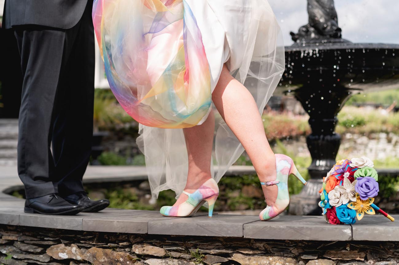 O fotografie de nuntă strălucitoare și colorată cu o rochie de mireasă curcubeu, pantofi și un buchet multicolor.  de Jay Page Photography