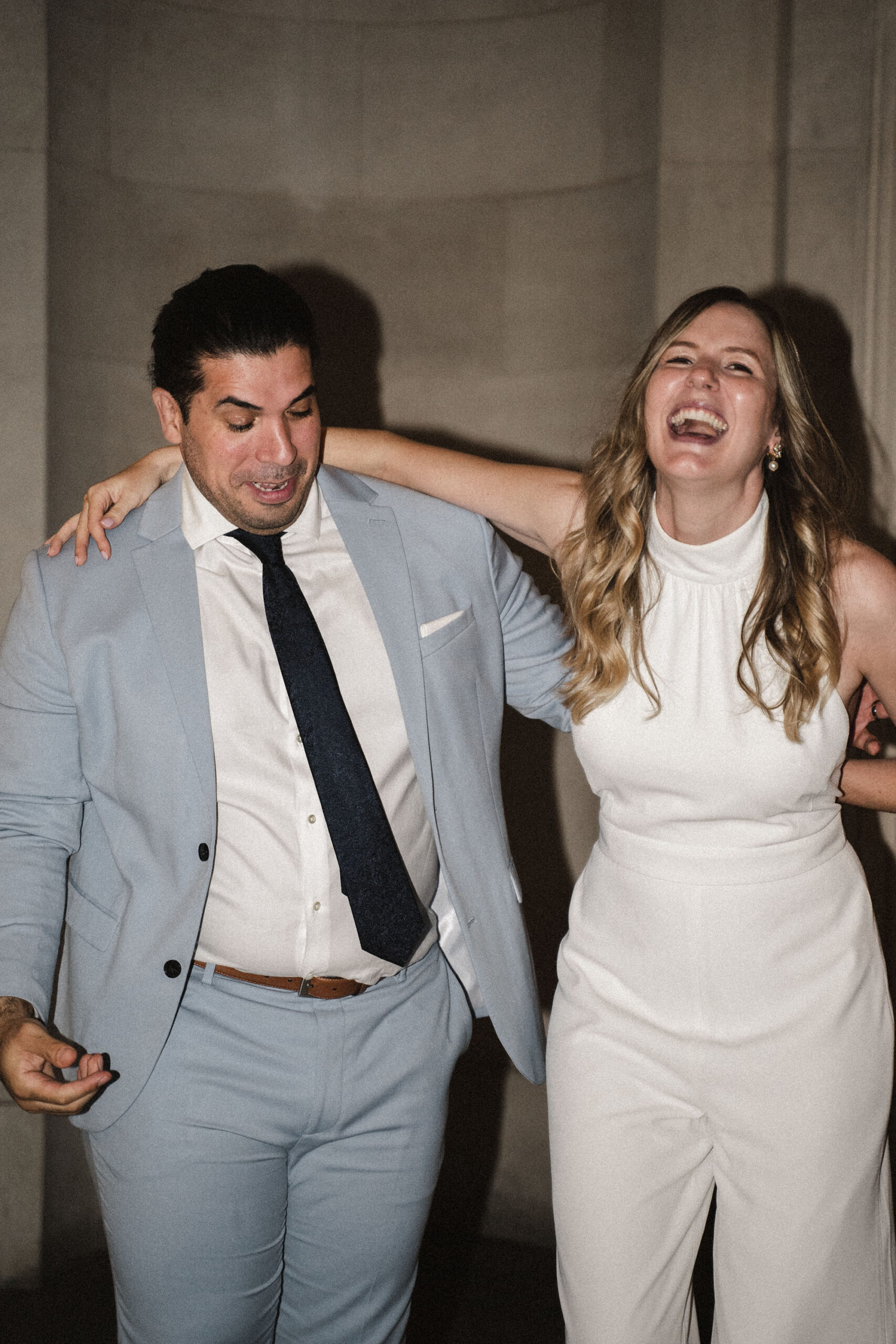 Modern wedding photography of a couple of newlyweds. He's in a pale grey blue suit with navy tie, and she's in a white jumpsuit. By Karolina Photography