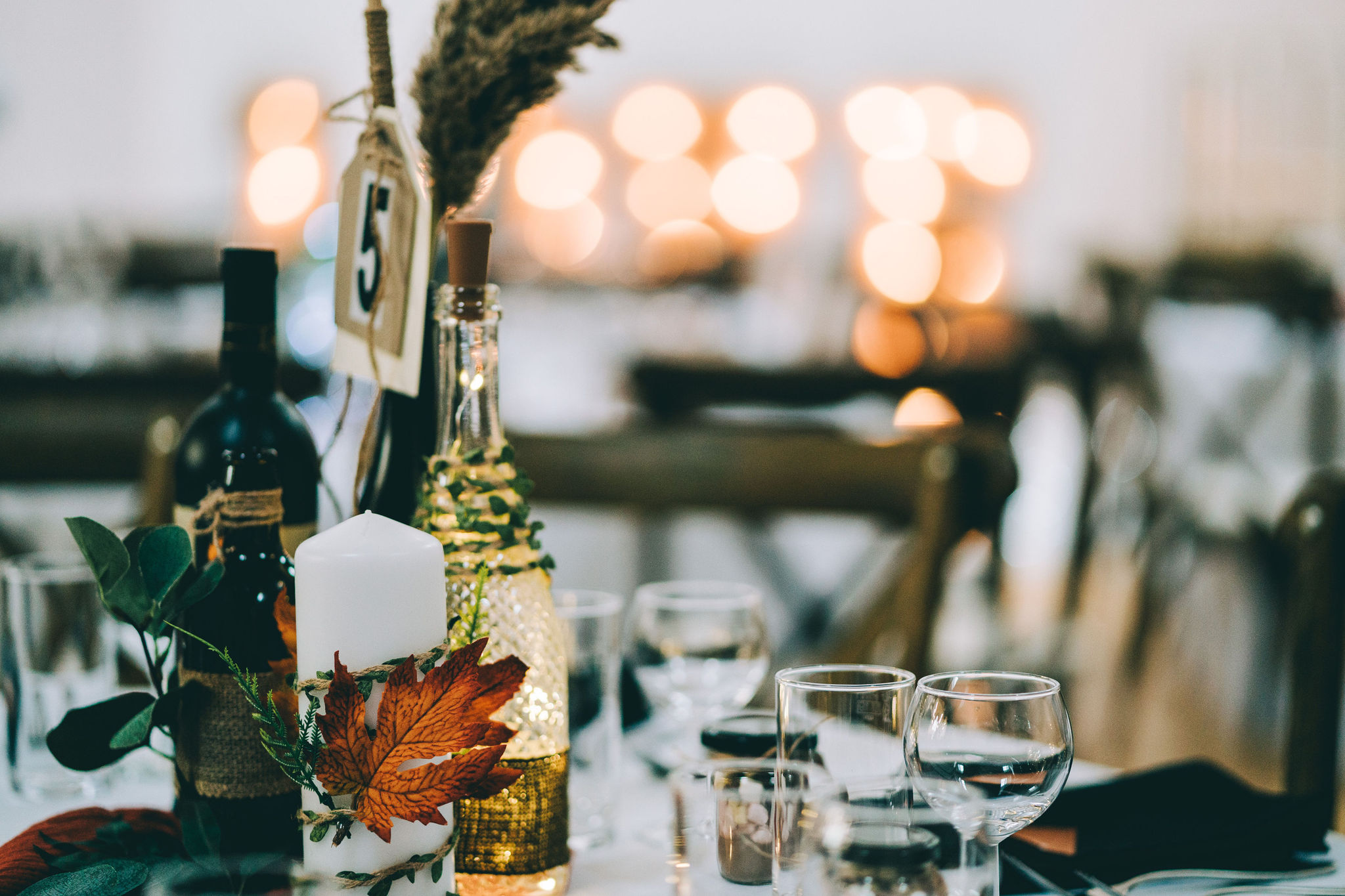 Autumnal wedding table with rustic leaf decorations, fairy lights in fancy bottles and lights glowing in the background