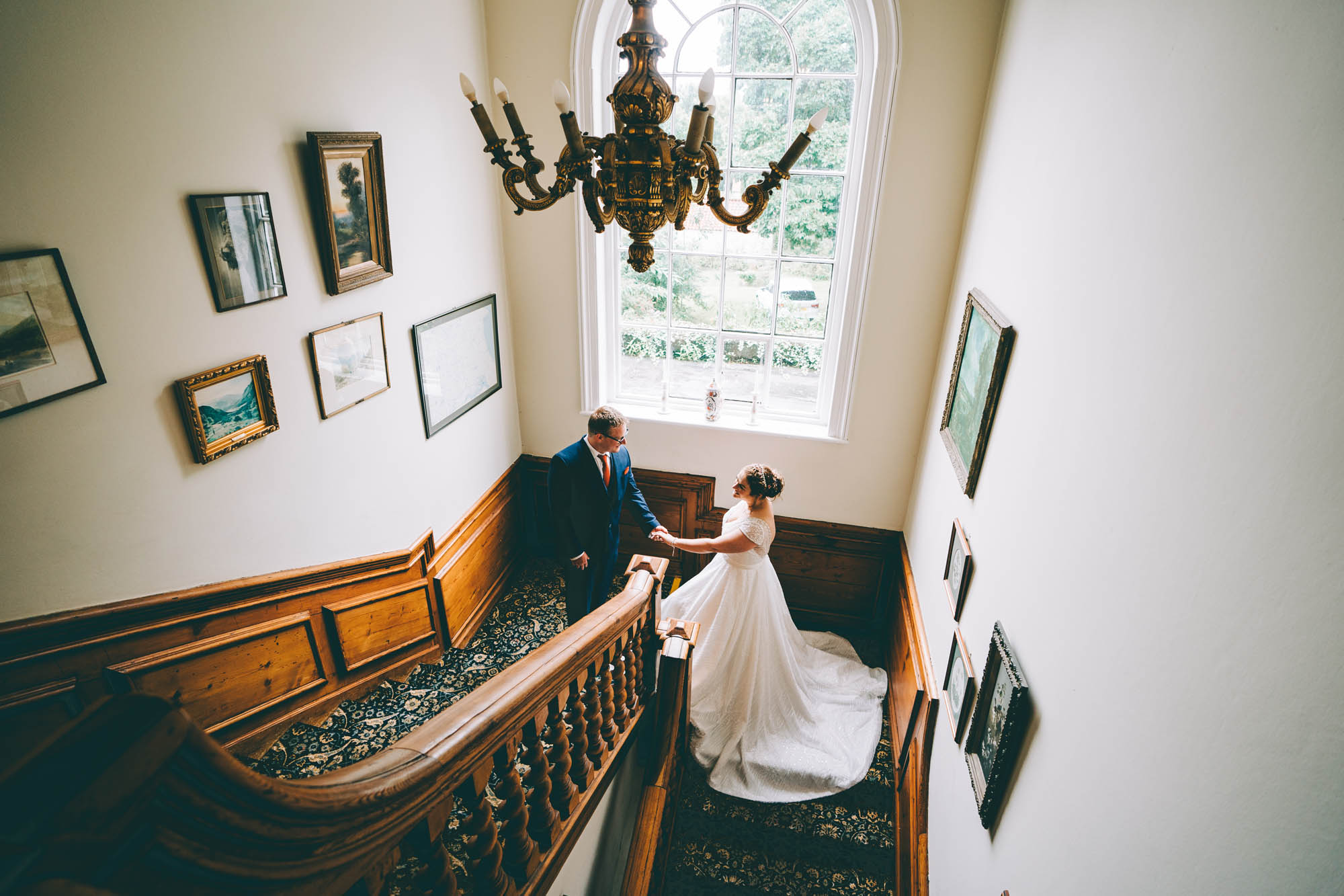 A bride and groom hold hands on a grand staircase in a stately home wedding venue. By Abraham Photography