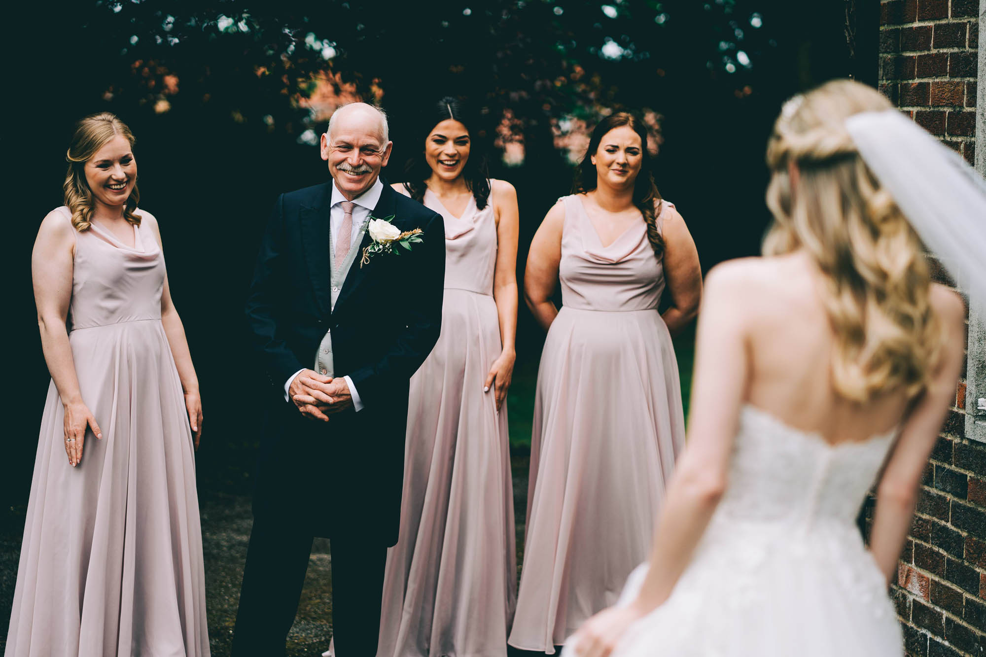 The father of the bride and three bridesmaids see the bride in her dress for the first time. By Abraham Photography