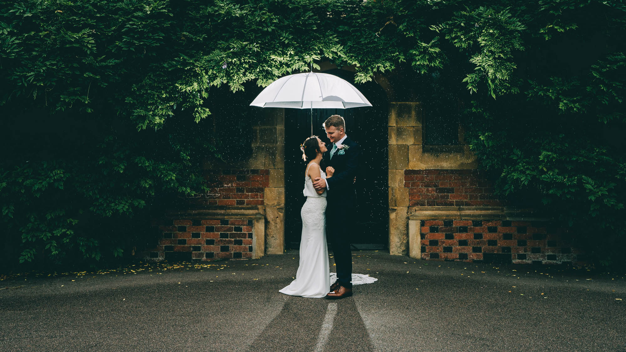 Beautifully lit wedding photo with a white umbrella. A bride and groom stand in a courtyard facing each other. By Abraham Photography