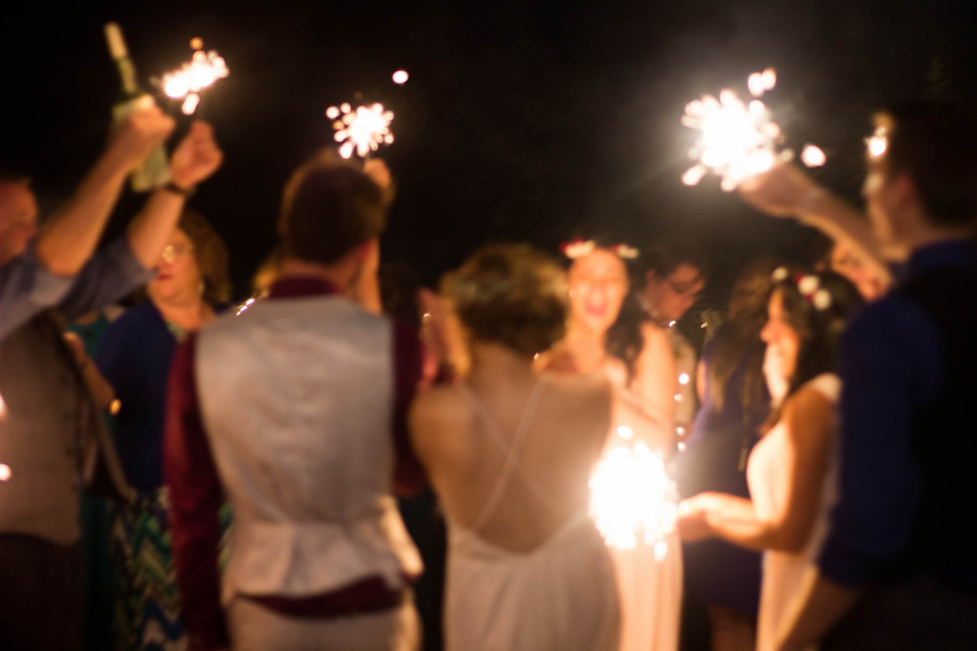 Wedding guests face each other holding sparklers at night