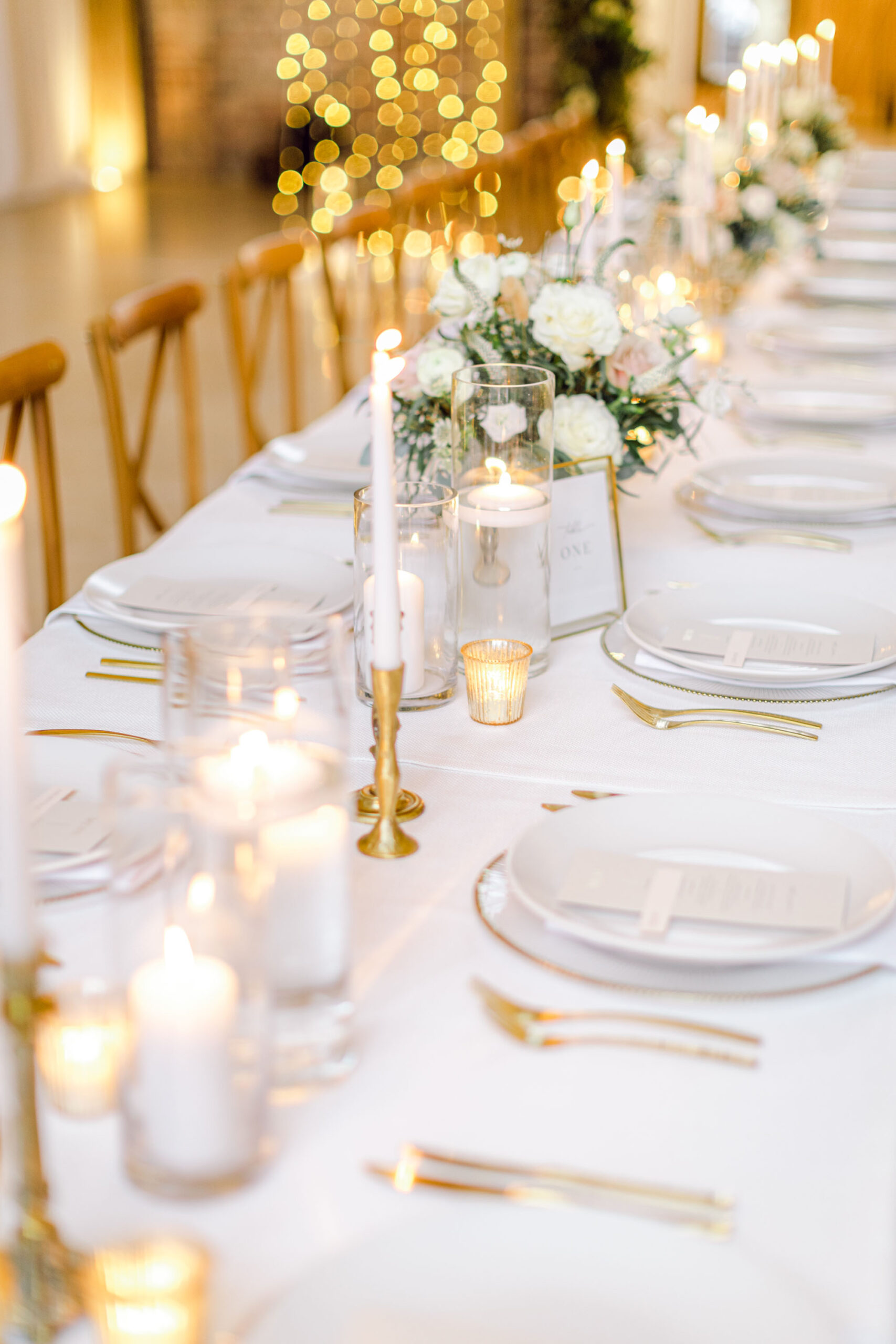 Twinkling floating candles line the centre of a luxury wedding table with gold cutlery and white plates. Styling by Illy Elizabeth Weddings. Photo by Natalie D Photography