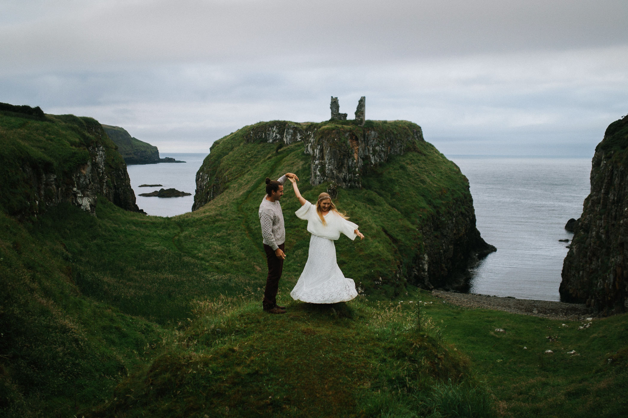 A couple dance on a grassy clifftop on the coast with the sea behind them. By Luke Flint Photography
