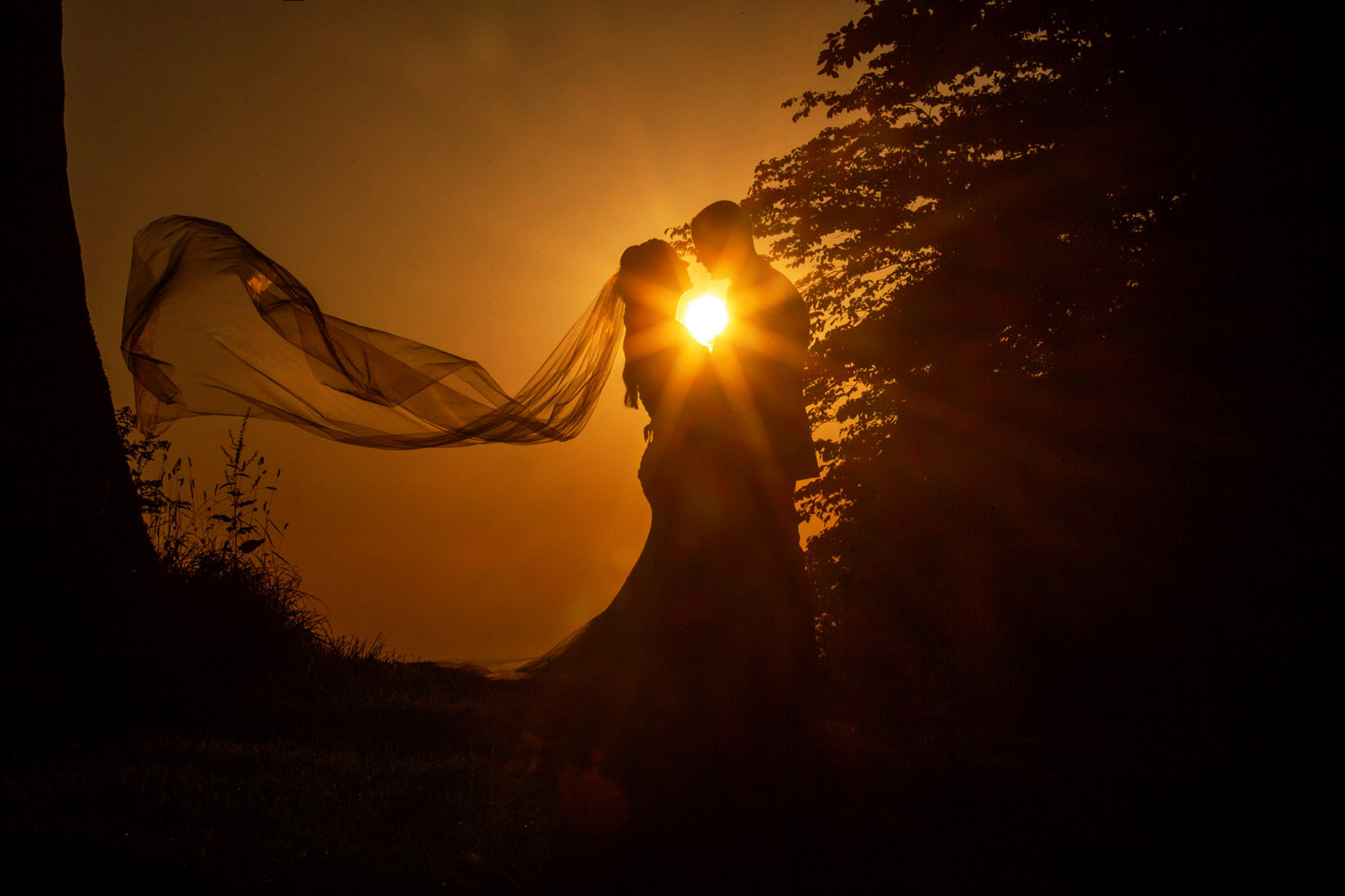 Beautiful sunset wedding photograph, with the sun flare between the couple. Captured by Martin Dabek Photography in B