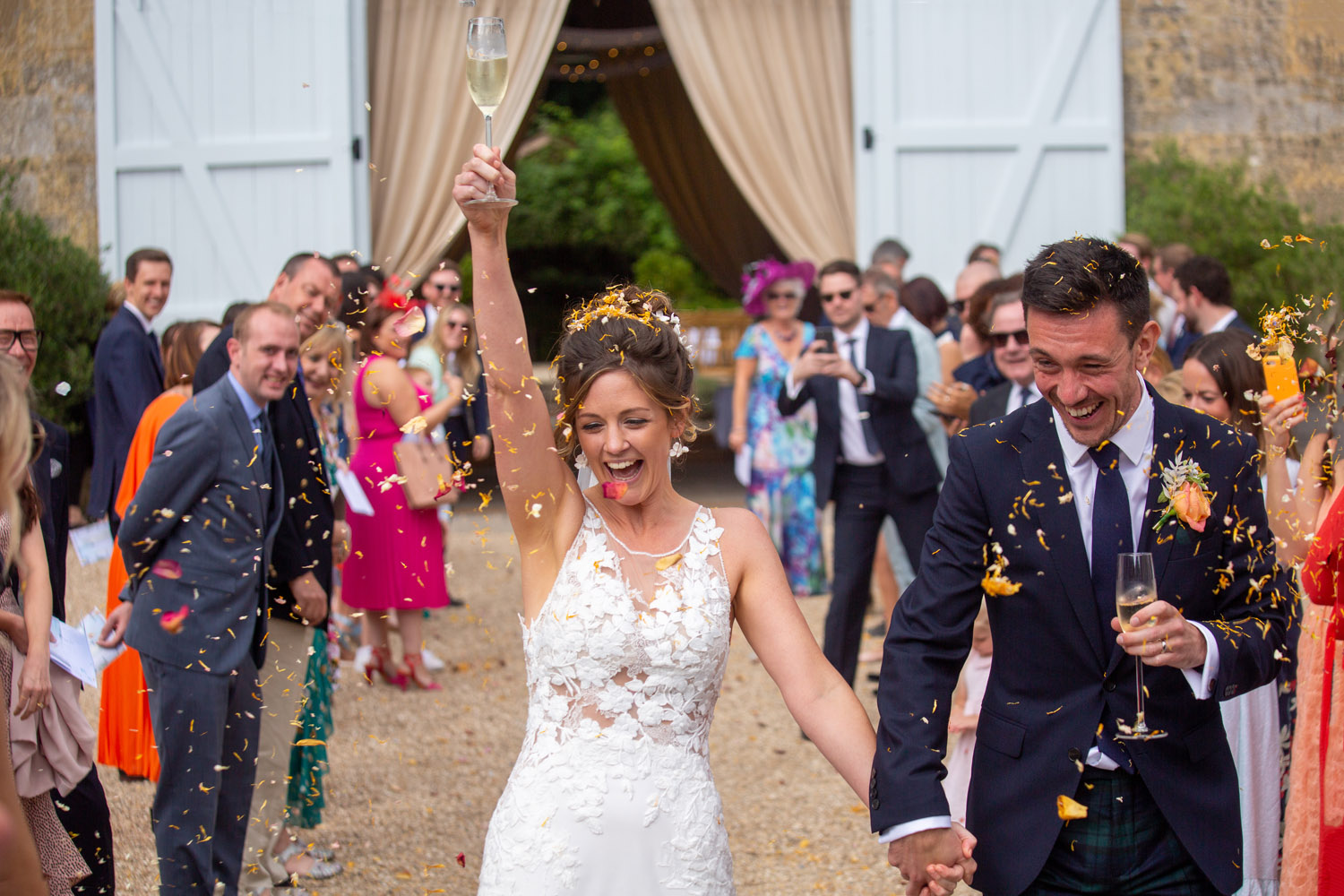 A bride celebrates with her hand raised as she and her groom complete the confetti walk after their wedding! With Somerset photographer Martin Dabek Photography, Bristol