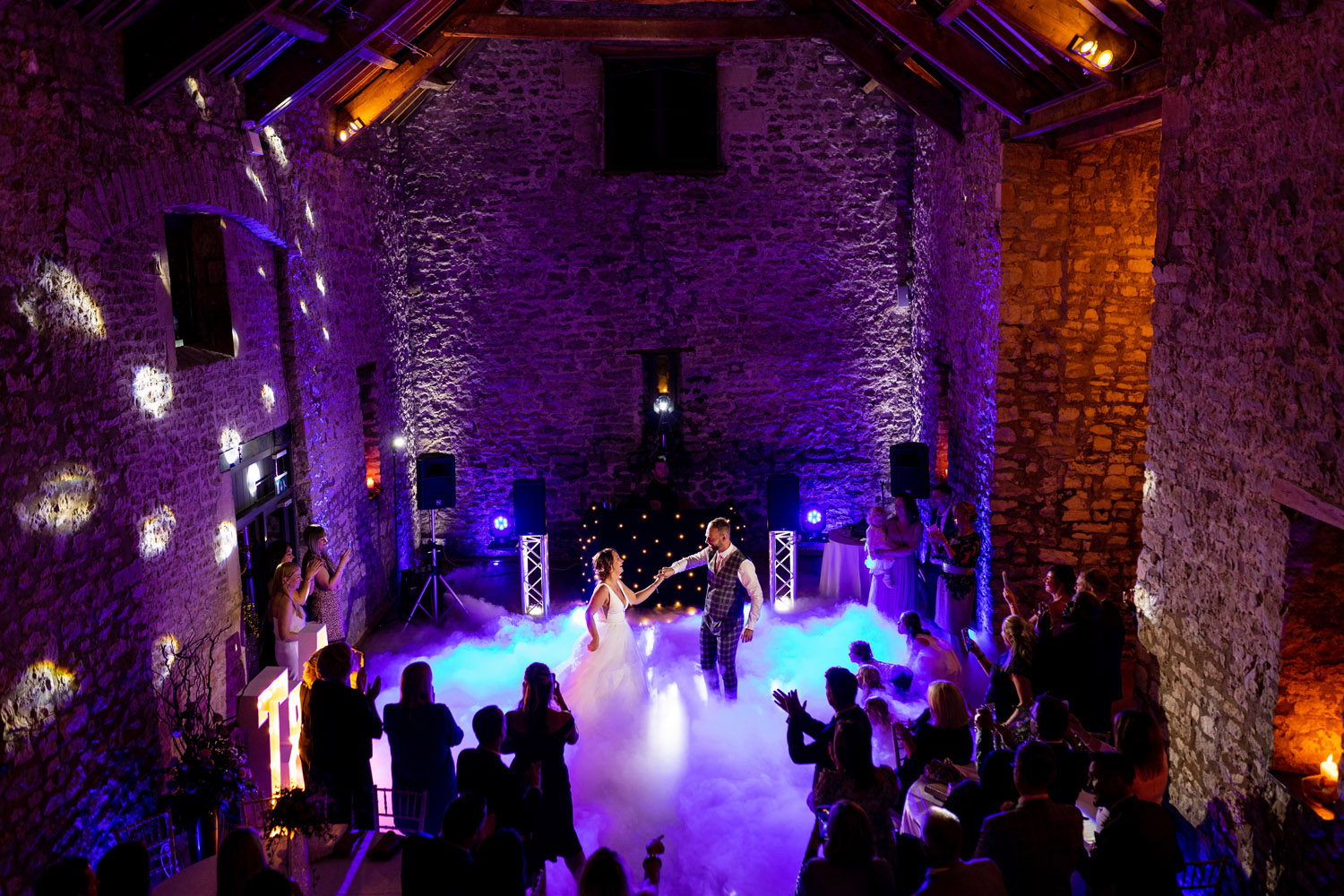 A bride and groom take the stage for their first dance. The venue is lit with purple lights and there's smoke filling the dance floor. With Martin Dabek Photography in Somerset