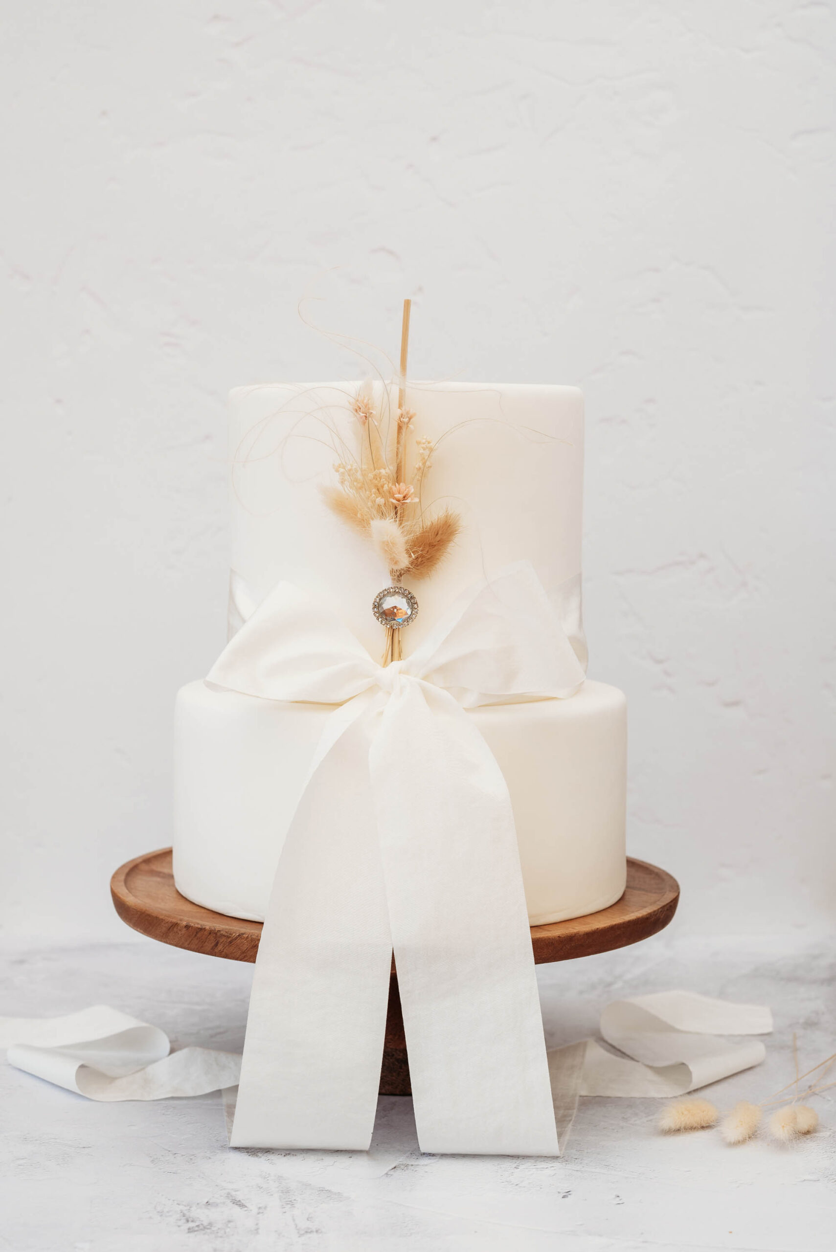 simple two tier modern white wedding cake with dried grasses and a wide silk ribbon, made by Cakes by Tasha
