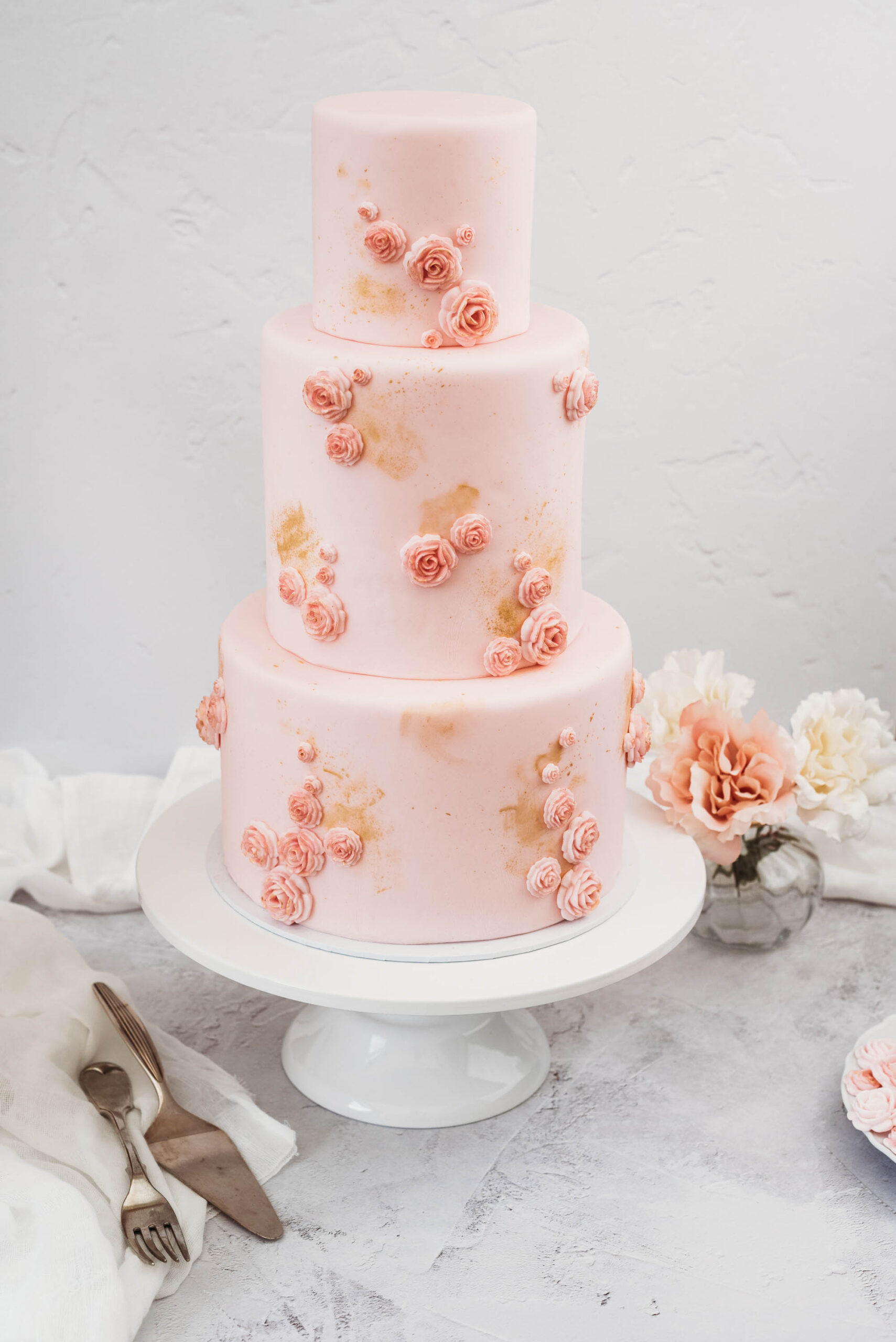 pink three tier wedding cake with delicate pink rose clusters and dashes of pretty gold to give a watercolour effect