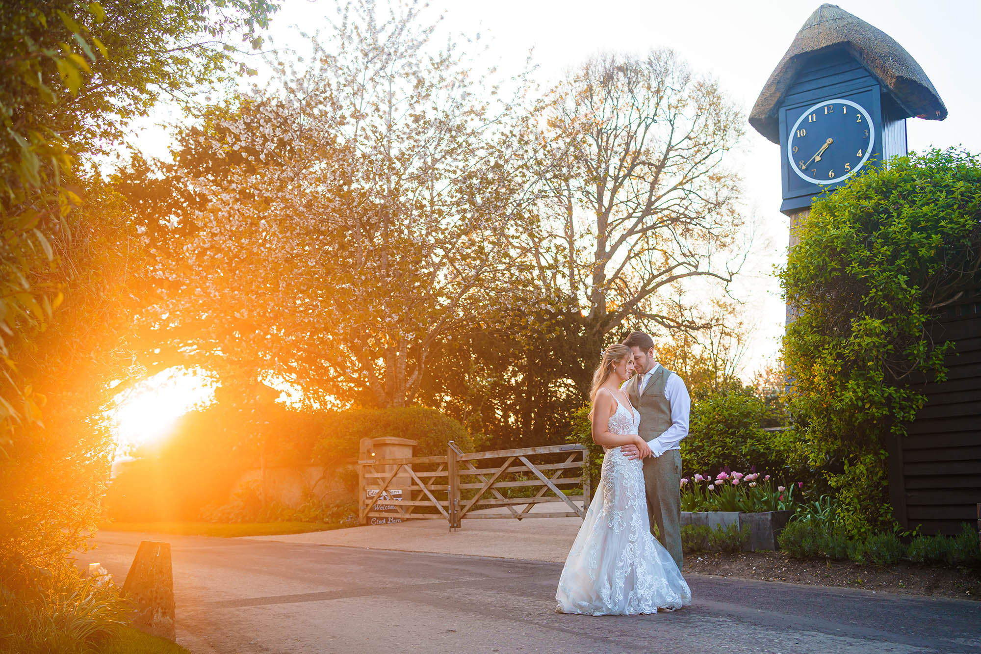 A bride and groom stand beside a clock tower as the sun sets. Image by Daniel Thomas Photography