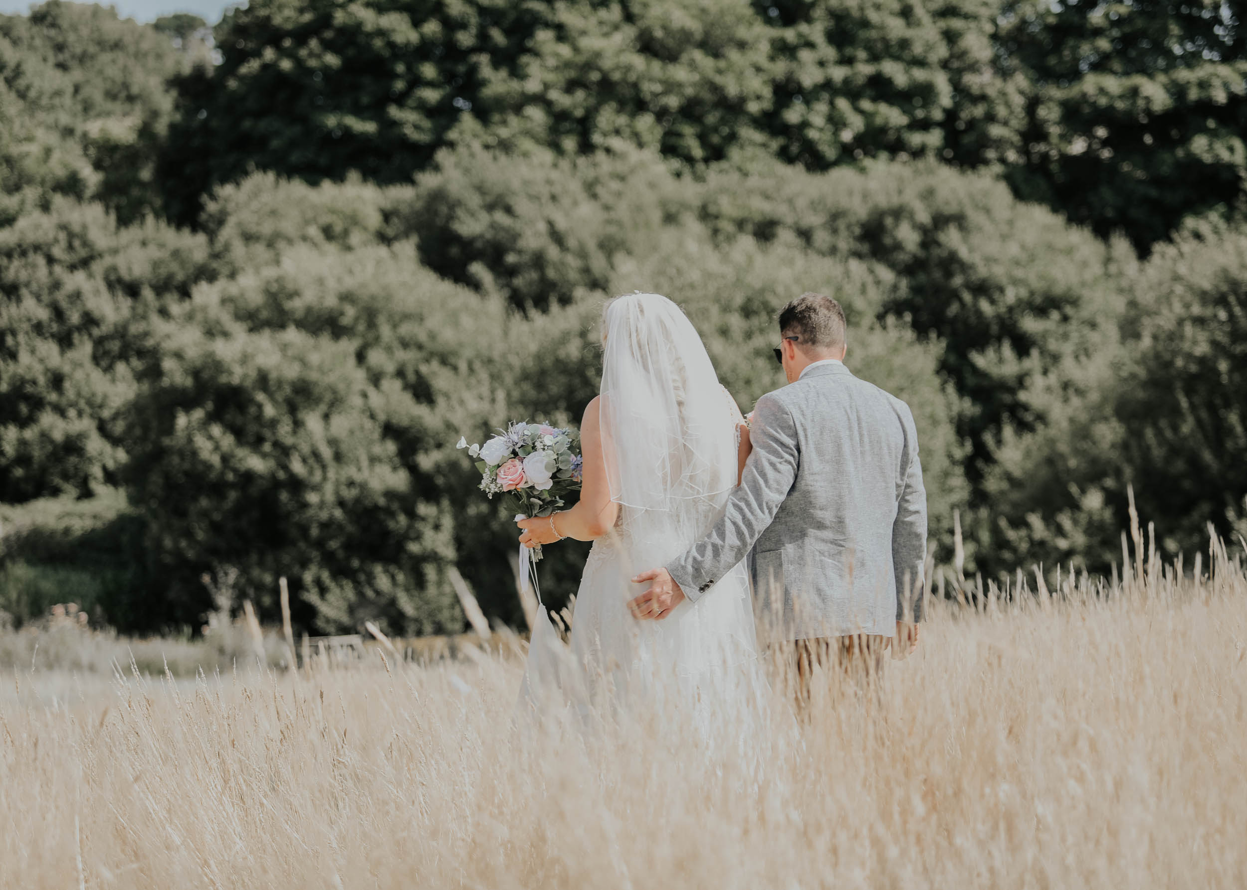 Newlyweds walking away from the camera through a corn field