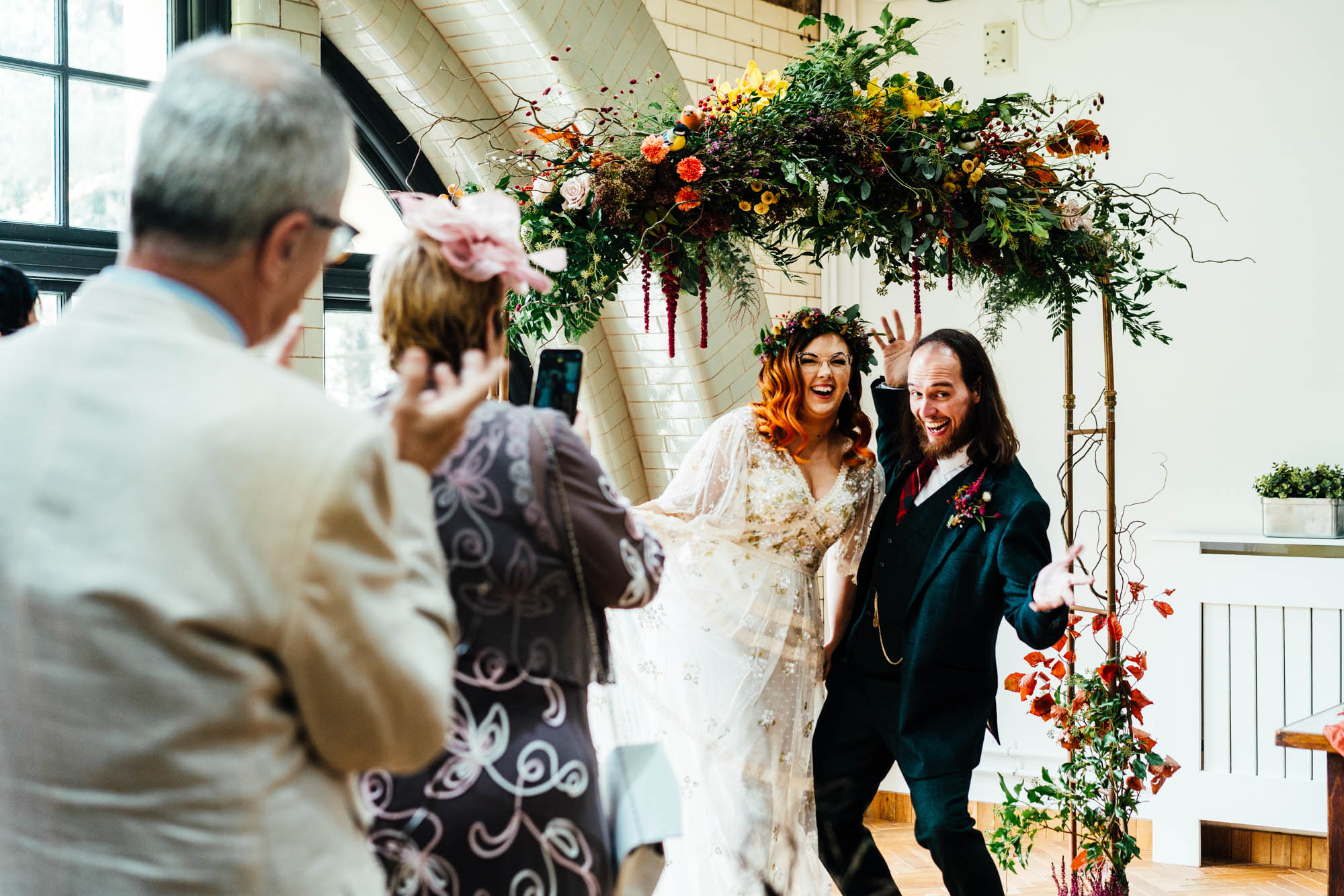 Alternative bride and groom posing for guest pics under a floral arch - by Hannah Hall Photography