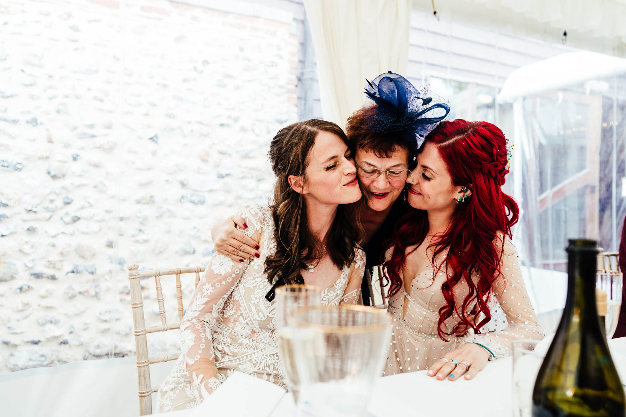 A guest leans over the shoulders of two brides for a magical group hug - by Hannah Hall Photography