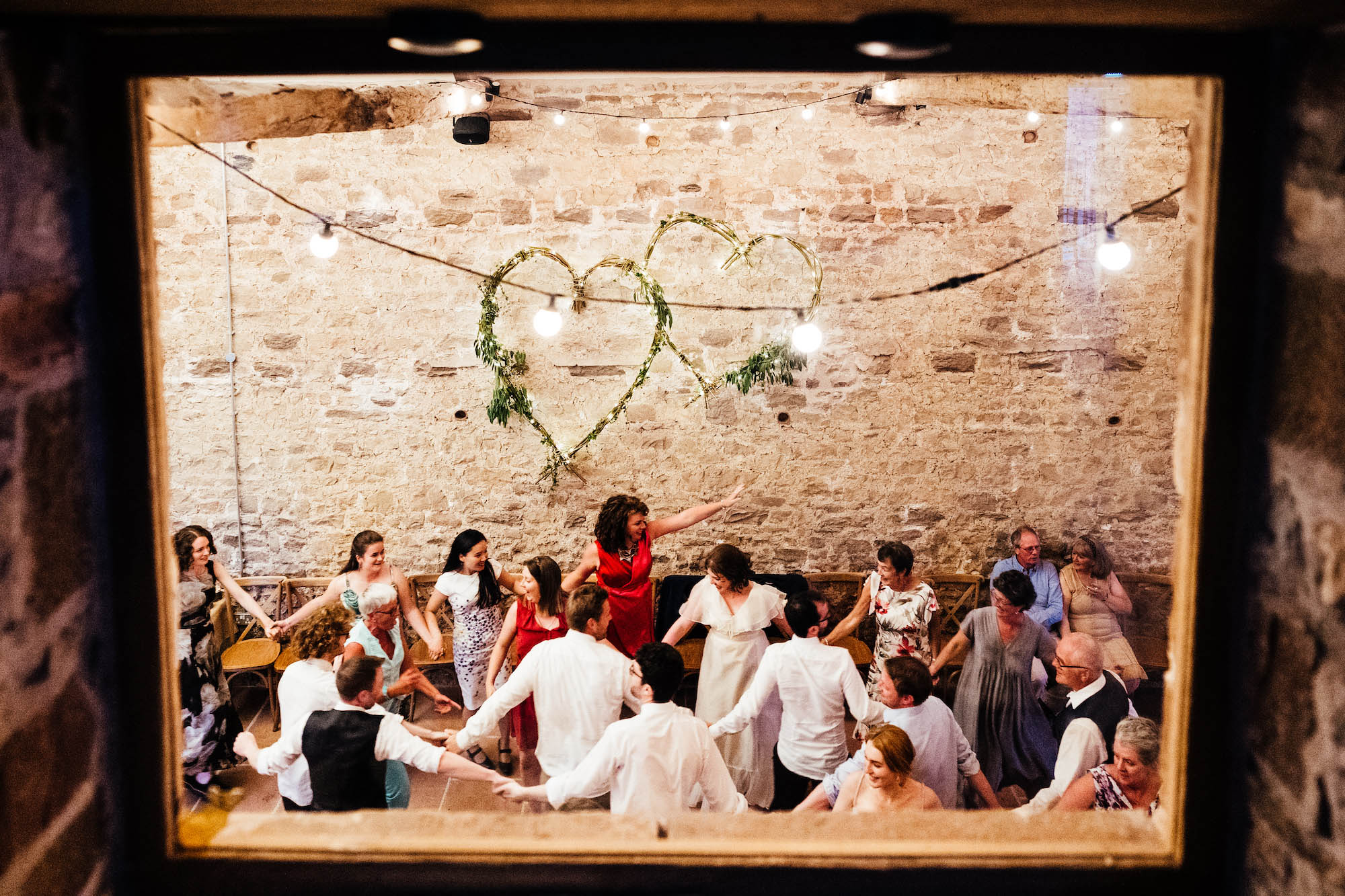 Looking through a barn window at guests celebrating a wedding - by Hannah Hall Photography