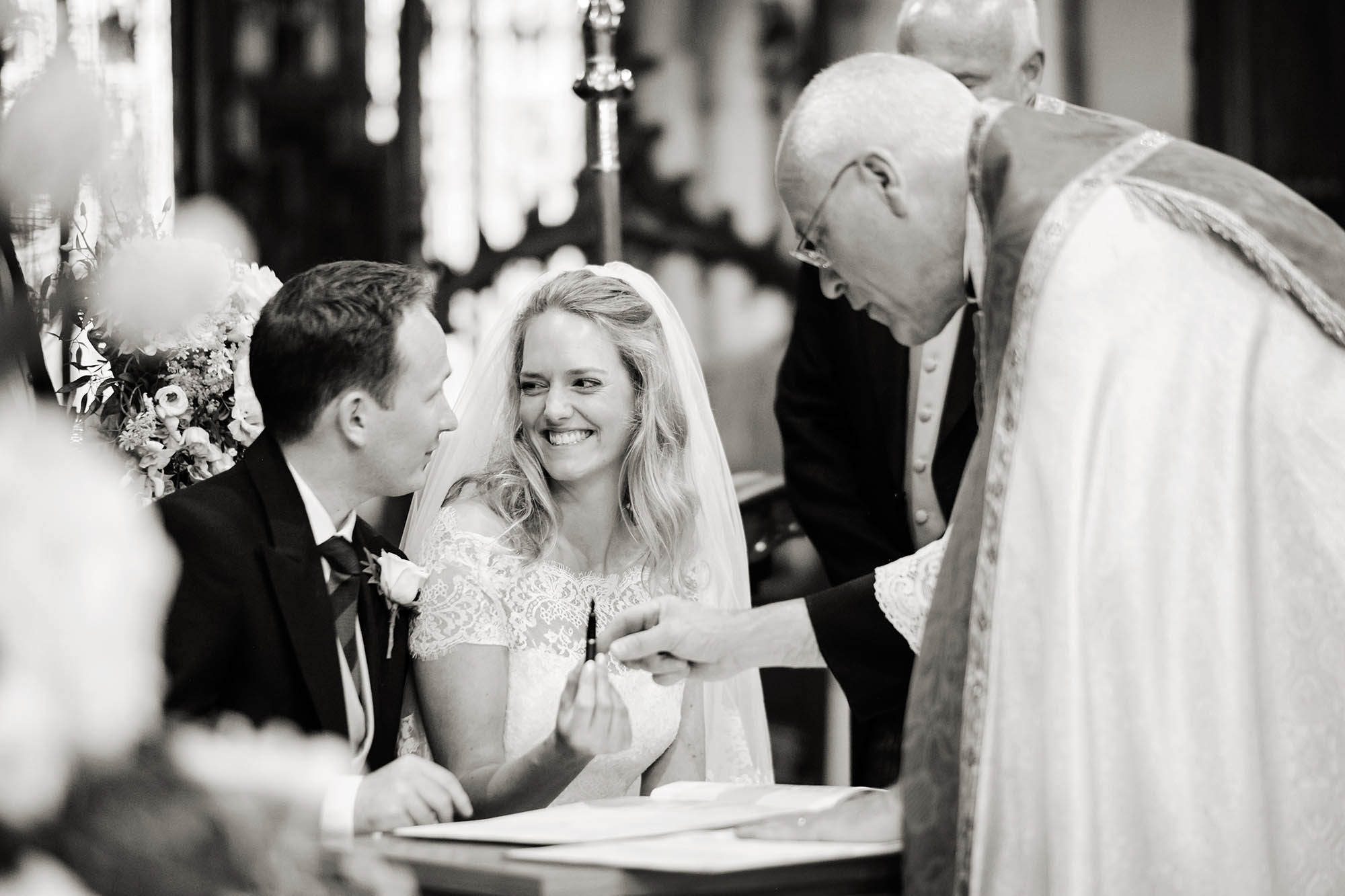 A bride smiles at her new husband as she hands the pen back to the priest after signing the marriage register - Sheffield wedding photographer John Mottershaw