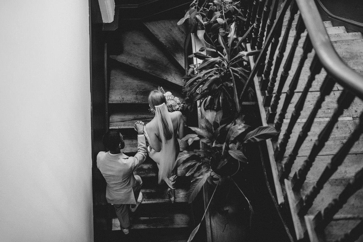 Elegant modern wedding photography by Ellie Gillard. A bride and groom ascend the stairs in a grand wedding venue. The photo is in black and white and taken from above.