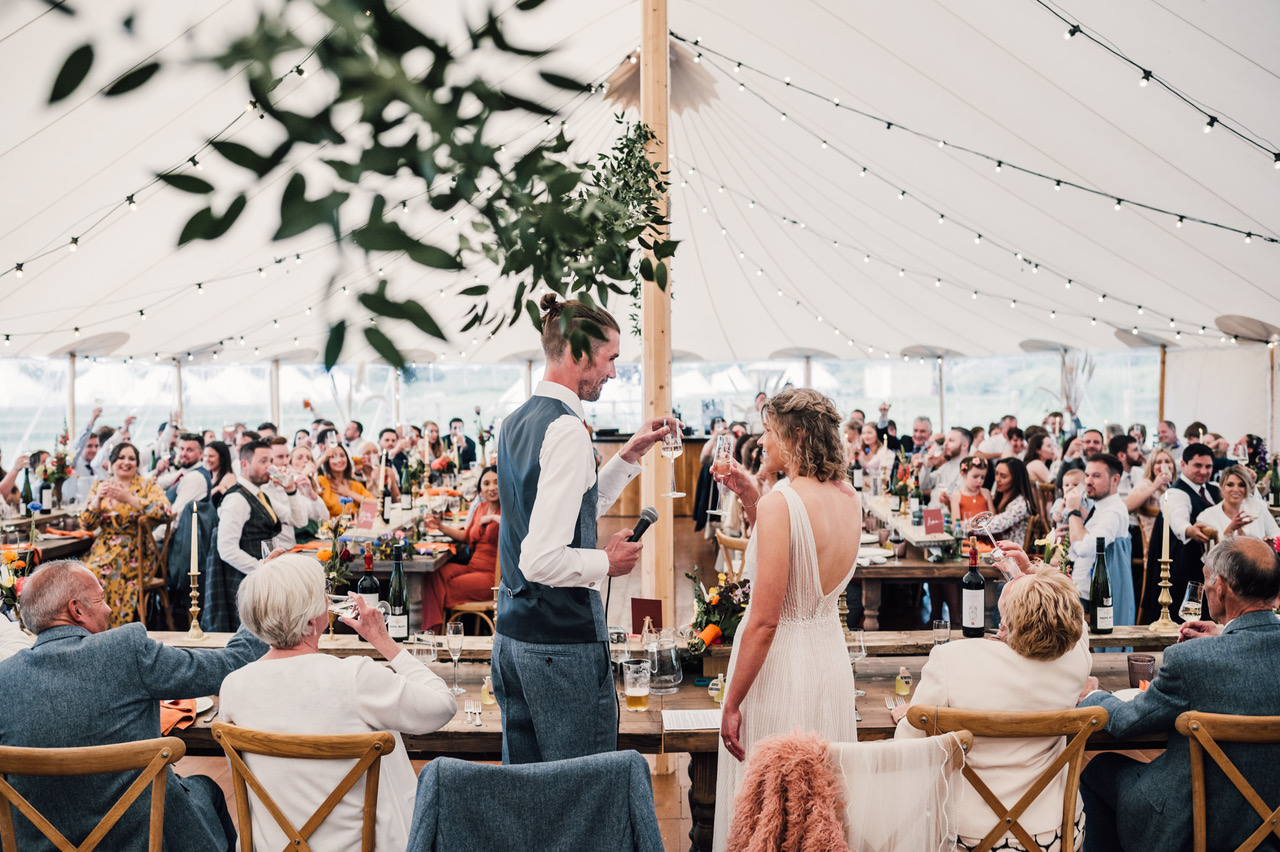 A couple in a wedding tent face their guests and make a toast. Damien Vickers Photography