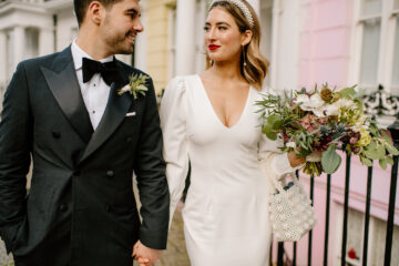 Modern elegant wedding photography of a groom in a tux and bow tie and a bride in a minimal dress with a plunge neckline. She's wearing a pearl headband and carrying a red and white bouquet. London wedding photographer Ellie Gillard