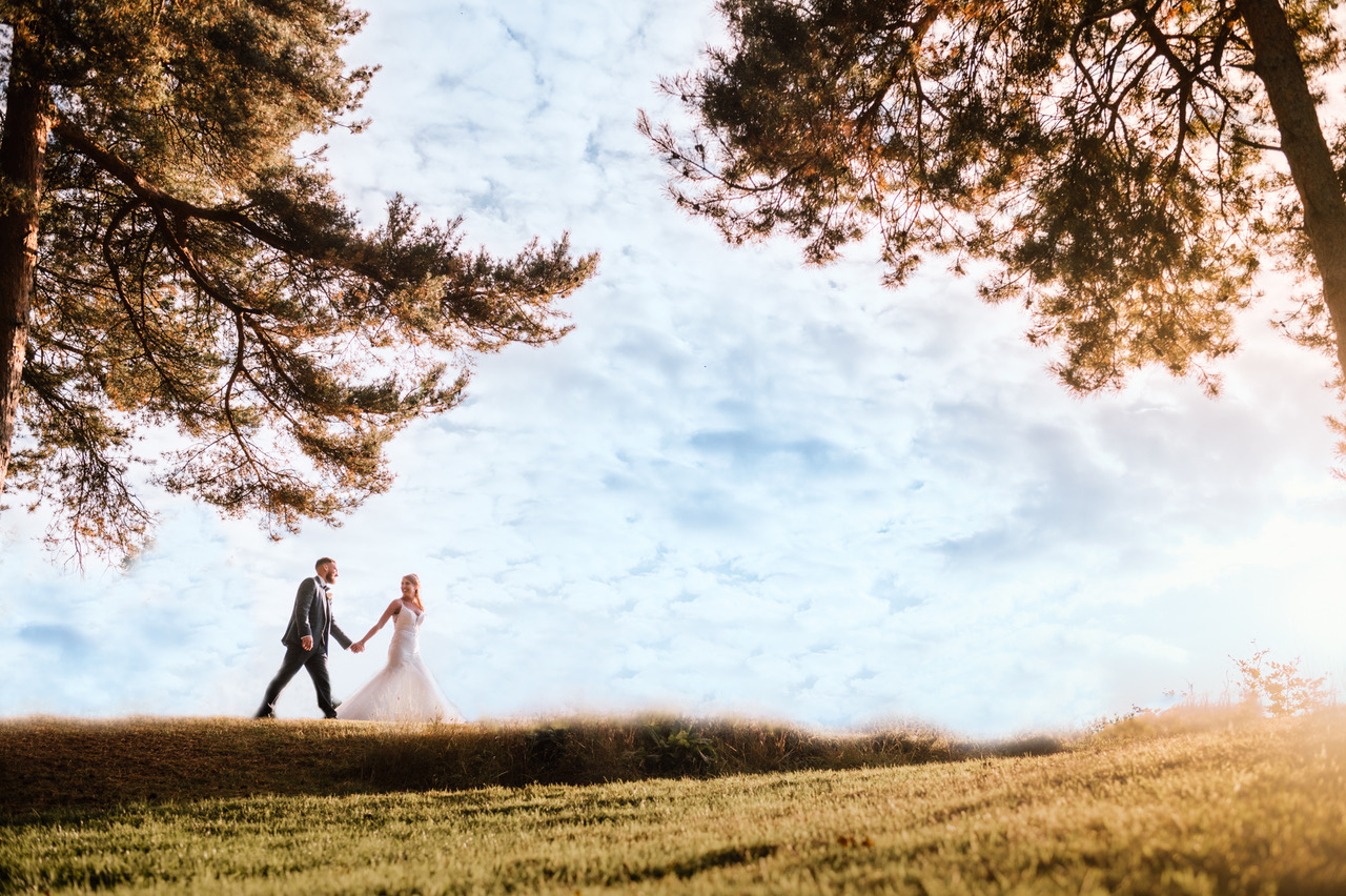 Landscape shot with a bride and groom crossing the field on the horizon. By Damien Vickers Photography