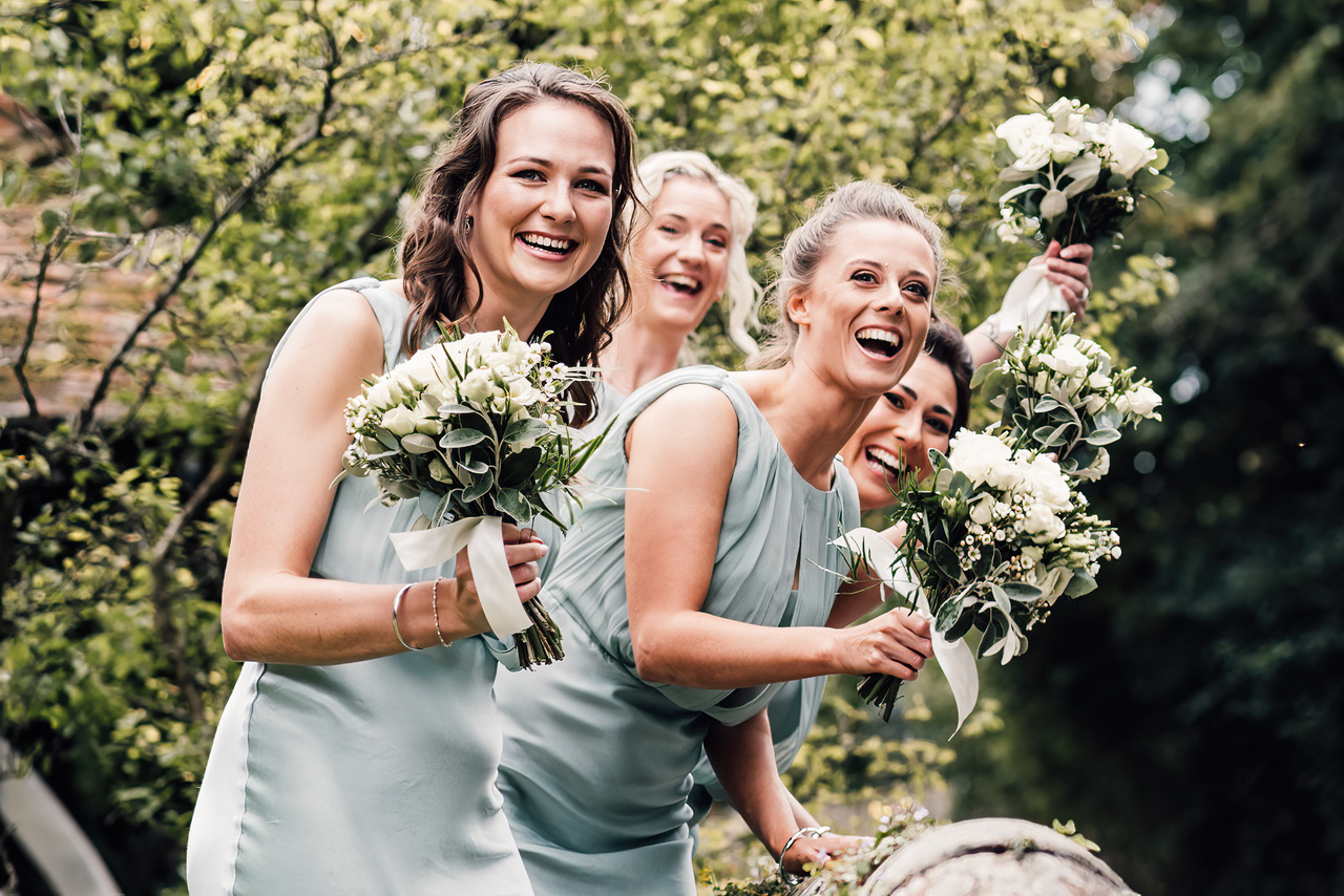 Bridesmaids holding their bouquets and laughing towards the camera. Damien Vickers Photography