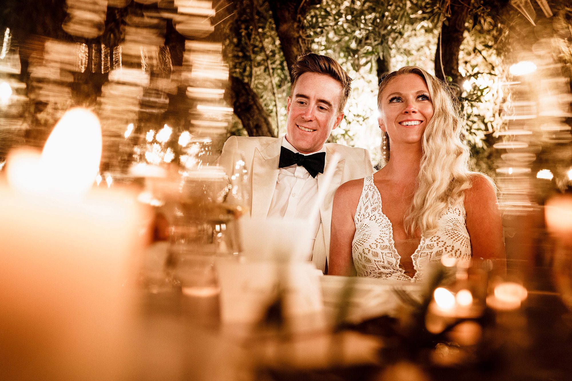 A bride and groom smiling as they listen to wedding speeches. Creative wedding photography by Stephen Walker